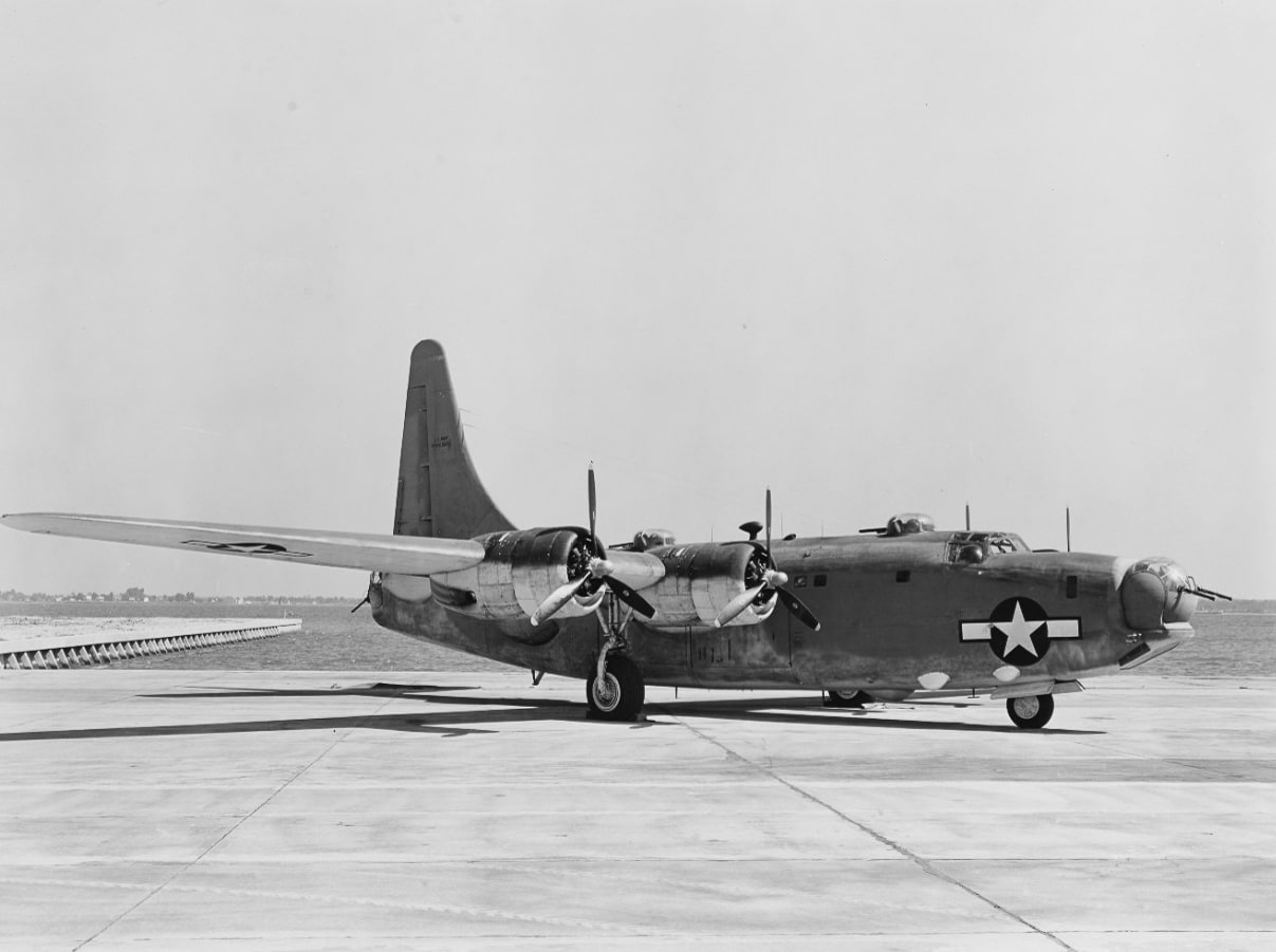 A U.S. Navy Consolidated PB4Y-2 Privateer is shown parked on the tarmac at Naval Air Station Patuxent River, Maryland, in 1944. This long-range patrol bomber was developed from the B-24 Liberator but featured a single tall vertical stabilizer instead of the twin tail design. The aircraft’s fuselage was lengthened to accommodate additional crew positions, including a flight engineer’s station. Designed for anti-submarine warfare and maritime patrol, the Privateer carried radar, depth charges, and heavy defensive armament. Its single tail improved stability during long over-water missions. The scene highlights the aircraft in testing and operational preparation before being deployed in the Pacific. The PB4Y-2 went on to serve in World War II, Korea, and even postwar roles such as weather reconnaissance.
