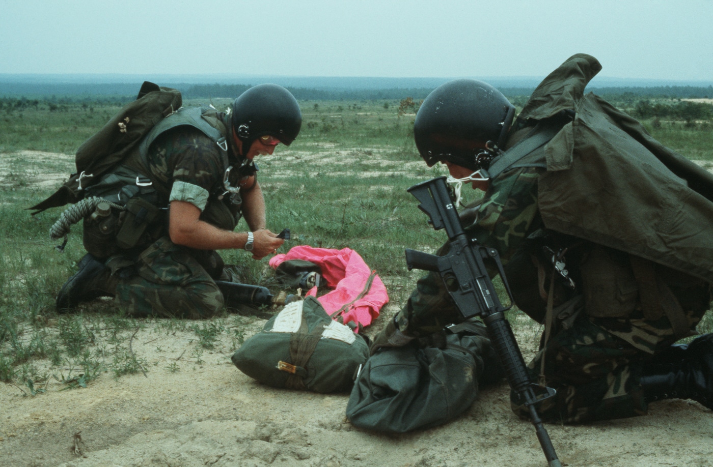 The image shows a U.S. Air Force combat control team during a 1979 training exercise, each operator carrying an XM177 Colt Commando CAR-15 rifle. The carbines are equipped with short 10–11.5 inch barrels, long moderator muzzle devices, and two-position collapsible aluminum stocks. Standard 20-round 5.56mm magazines are visible in several rifles, with some personnel carrying gear pouches and radios. The team is arranged in a tactical formation on open terrain, suggesting a field maneuver or insertion drill. Their uniforms are olive drab with standard issue web gear of the late 1970s. This description includes optimized terms such as XM177, Colt Commando, CAR-15, Air Force combat control, 5.56mm carbine, and 1979 training exercise for accessibility and search indexing.
