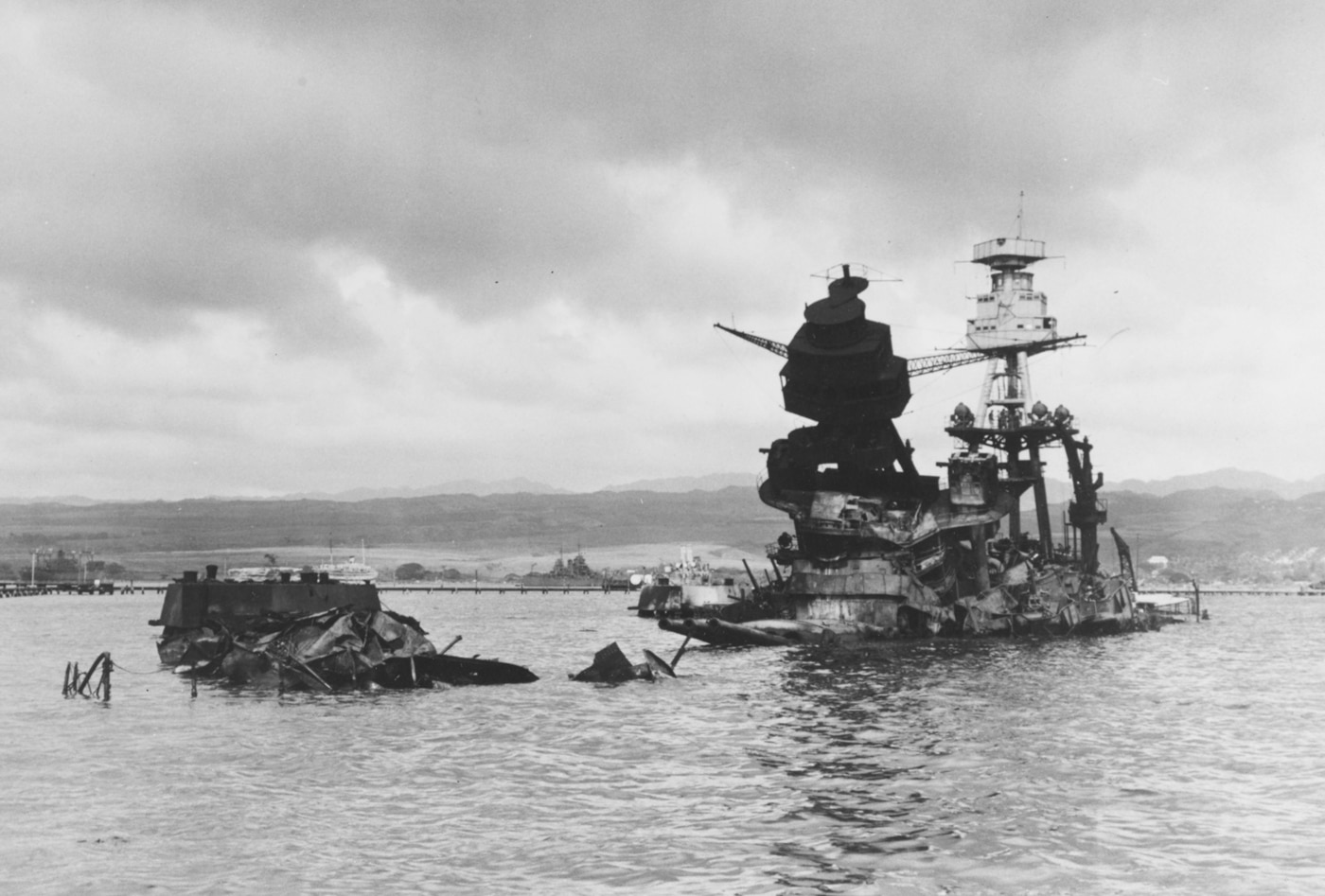 The photograph shows the wreck of USS Arizona (BB-39) in Pearl Harbor on December 10, 1941, three days after the Japanese attack. The battleship’s hull rests beneath the shallow water, while her superstructure remains above the surface, heavily damaged and blackened from fire. Smoke still lingers over parts of the wreck, and debris can be seen scattered across the water. Arizona was hit by armor-piercing bombs that ignited her forward magazine, causing a catastrophic explosion. The blast destroyed the ship and killed more than 1,100 crewmen, making it the single deadliest loss of life aboard a U.S. warship. This photo documents the immediate aftermath of her sinking, capturing both the destruction and the immense human cost. The image has since become one of the defining visuals of Pearl Harbor.