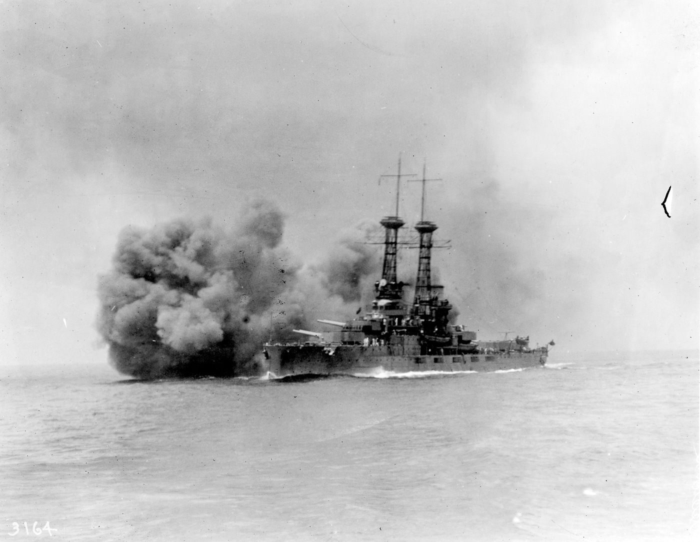 The photograph shows USS Delaware (BB-28), an early U.S. Navy dreadnought battleship, firing her main guns during a training exercise after World War I. The ship’s massive turrets unleash blasts of flame and smoke as shells are fired, with shockwaves visible across the water. Delaware was one of the original members of Battleship Division Nine, which operated alongside the British Grand Fleet during the war. Her design reflected the early dreadnought era, with a uniform heavy gun armament replacing the mixed calibers of pre-dreadnought battleships. This postwar image captures the impressive firepower that defined these ships, even as naval technology quickly advanced. Although she never fought in a decisive battle, Delaware symbolized America’s growing naval strength in the early 20th century. The photo highlights the destructive capability and imposing presence of early dreadnought battleships.