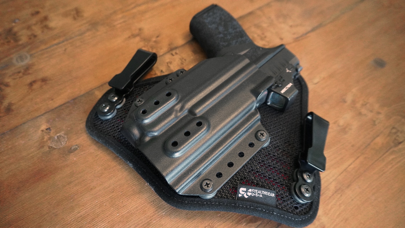 Close-up photograph of the StealthGearUSA Ventcore 2.0 holster showing the optics cut designed for pistols equipped with red dot sights. A Springfield Armory Hellcat Pro with a mounted optic is partially inserted to demonstrate compatibility. The cut in the Kydex shell allows the optic to sit above the slide without interference. The rest of the holster maintains full contact with the firearm for retention. Edges are smooth, with ventilation holes visible in the padded backing. This detail highlights the holster’s ability to handle modern concealed carry setups. The image emphasizes fit and optic clearance.