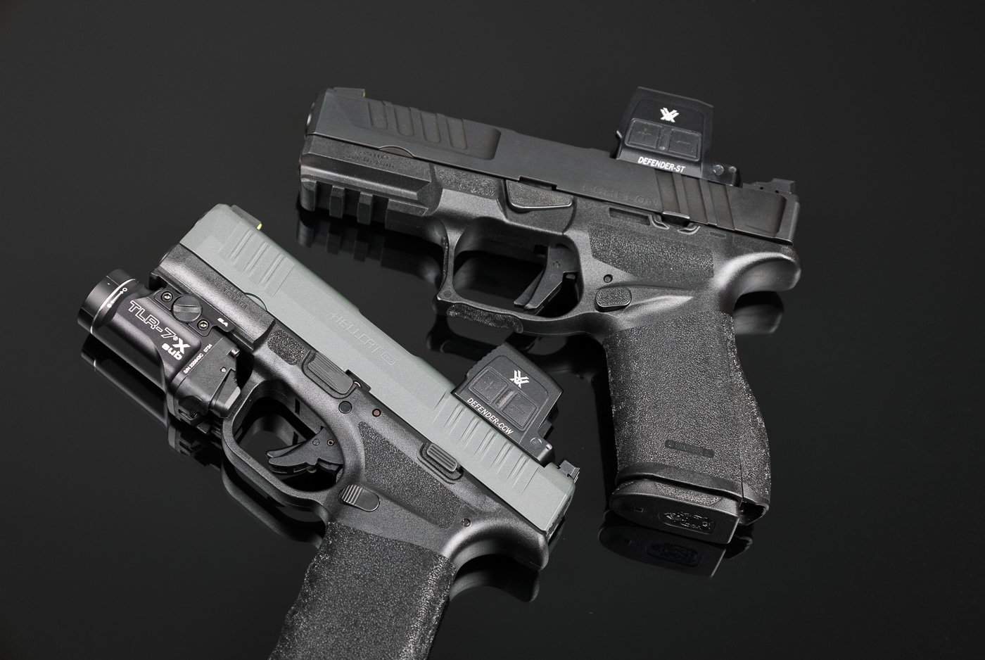 Image of two handguns displayed side by side on a flat surface, both fitted with Vortex Defender Enclosed optics. The compact Hellcat Pro pistol shows the smaller CCW variant of the enclosed sight, designed for concealed carry. The duty-sized Echelon 4.0C pistol is topped with the Defender-ST, which has a larger lens for faster target acquisition. Both optics have black anodized aluminum housings with solar panels visible on the top section. Their design emphasizes reliability, closed emitter protection, and compatibility with common mounting footprints. The pistols are photographed clearly, showing how the optics sit low on the slides. This setup demonstrates practical pairing options for different firearm roles.