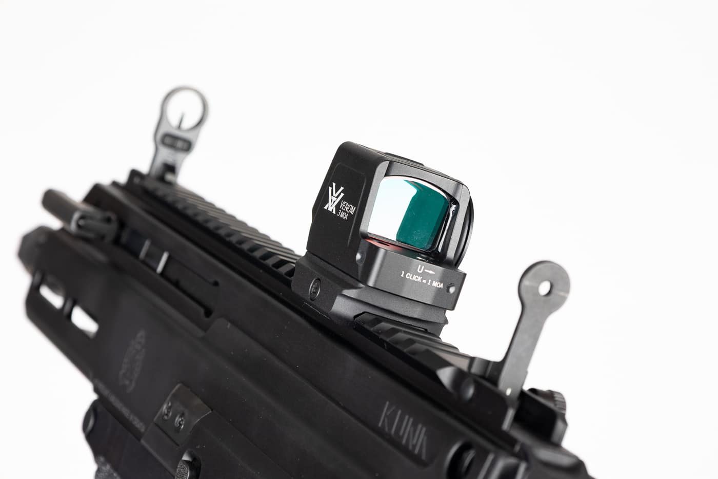 Close-up image of a Springfield Armory Kuna pistol with a Vortex Venom Enclosed 3 MOA red dot sight mounted on a low Picatinny adapter and the iron sights deployed for co-witness. The 3 MOA reticle appears as a small, precise red dot visible in the optic window, while the flip-up iron sights are raised behind the sight allowing a backup aiming method. The enclosed-emitter housing is visible and shows the sealed, dust-resistant construction that prevents grit and debris from obscuring the dot. The side-loading CR2032 battery tray and top brightness buttons can be seen, indicating easy maintenance without removing the optic. This image supports the Vortex Venom Enclosed red dot sight review by illustrating how the closed-emitter design and DeltaPoint Pro-compatible footprint integrate with a railed pistol. The composition emphasizes reliability, co-witness capability, and readiness for defensive or duty scenarios.