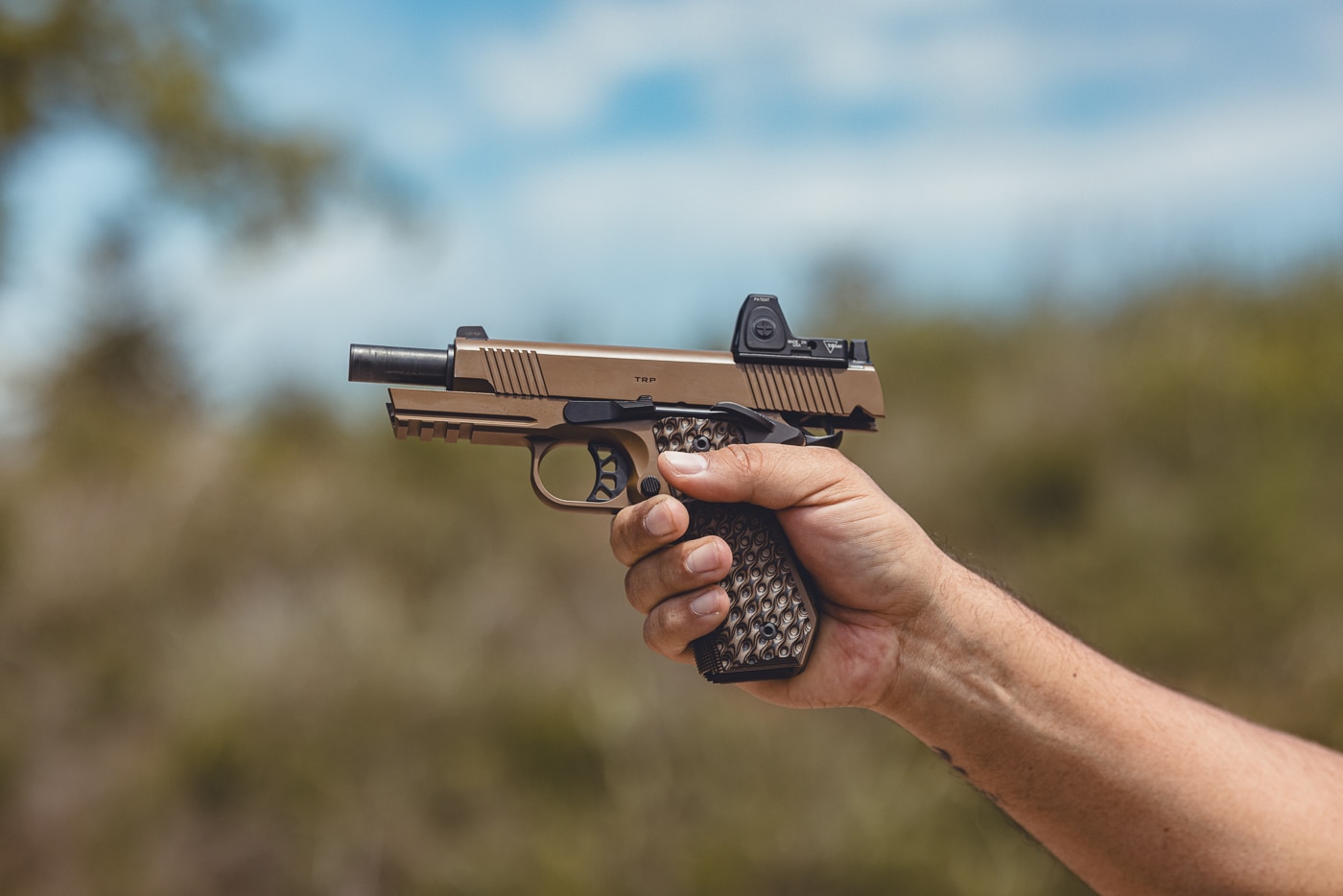 This photo shows the author holding a Springfield Armory 1911 TRP AOS pistol fitted with a red dot sight mounted on the slide. The handgun is gripped firmly with both hands, displaying proper handling technique. The optic is securely installed using the Agency Optic System plate, sitting flush with the slide. Visible details include the pistol’s textured G10 grips, matte finish, and skeletonized trigger. The image demonstrates how the TRP AOS combines the ergonomics of a traditional 1911 with the speed and accuracy of modern optics. This highlights the practical application of the AOS system in real-world use.