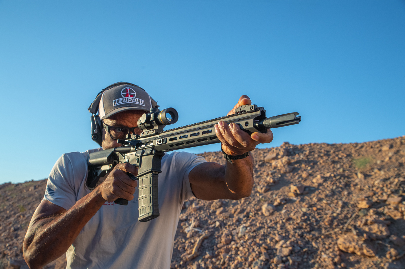 A shooter is pictured firing the new Springfield Armory SAINT Victor 2 rifle at an outdoor range. The firearm being tested is the 14-inch pinned and welded version chambered in 5.56 NATO. The shooter has the rifle shouldered and is engaging targets downrange, demonstrating stability and control. Visible details include the free-float rail with M-Lok slots, the B5 Systems stock, and low-profile iron sights mounted on the top rail. The rifle is equipped with a four-prong flash hider, a feature unique to this updated line. The image captures live-fire testing to highlight accuracy, recoil management, and overall ergonomics. This setup represents one of Springfield Armory’s 2025 SAINT Victor releases, designed to offer reliability and performance at a mid-tier price point.