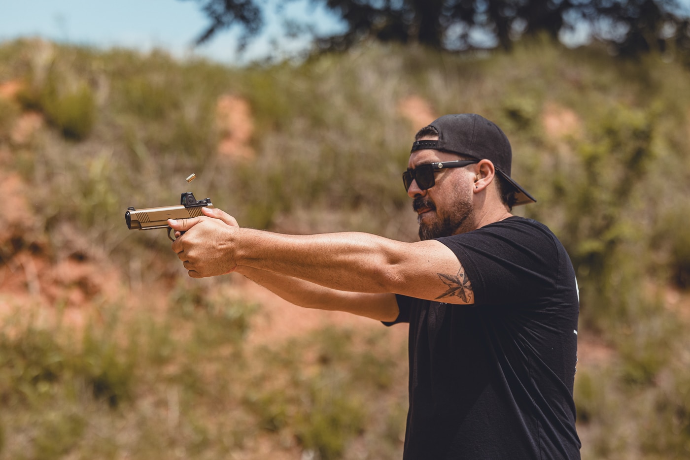 This photo shows the author shooting a Springfield Armory 1911 TRP AOS equipped with a red dot sight. The pistol is in live fire, with the shooter maintaining a solid two-handed grip and forward stance. The mounted red dot optic sits low on the slide, providing fast target acquisition. Visible details include the pistol’s serrations, G10 grips, and forged frame design. The outdoor range environment reinforces the live training context. This image highlights how the TRP AOS functions with modern optics under real shooting conditions.