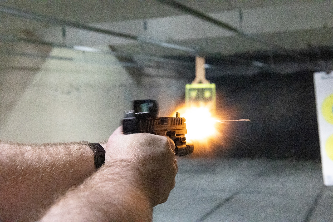 Photo of the author firing a Springfield Armory Echelon pistol equipped with the Vortex Venom Enclosed red dot sight at an indoor shooting range. The shooter is pictured extending the handgun toward the target under dim lighting conditions. The optic’s red dot remains visible in the window, helping the shooter acquire the sight picture quickly. The enclosed design of the optic prevents interference from airborne grit, dust, and ejected brass flying into the lane. The metal housing is visible but does not obstruct the shooter’s field of view. This image illustrates how the Venom Enclosed performs in practical, real-world shooting environments. The test emphasizes reliability, ease of use, and durability during recoil and extended sessions.