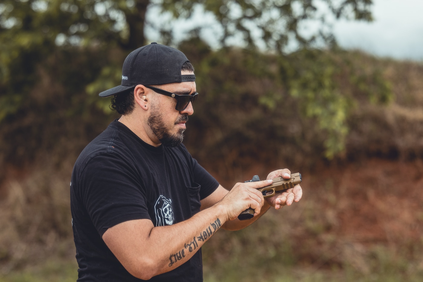 This image shows the author at an outdoor shooting range holding a Springfield Armory 1911 TRP AOS pistol. The firearm is equipped with a red dot sight, demonstrating the Agency Optic System in a live-fire environment. The shooter is positioned on the firing line, practicing target engagement with the upgraded 1911. The range setting includes ear protection, safety gear, and a standard target setup in the background. The pistol’s forged frame, G10 grips, and mounted optic are visible in use. This photo illustrates how the TRP AOS transitions from bench display to practical shooting performance.