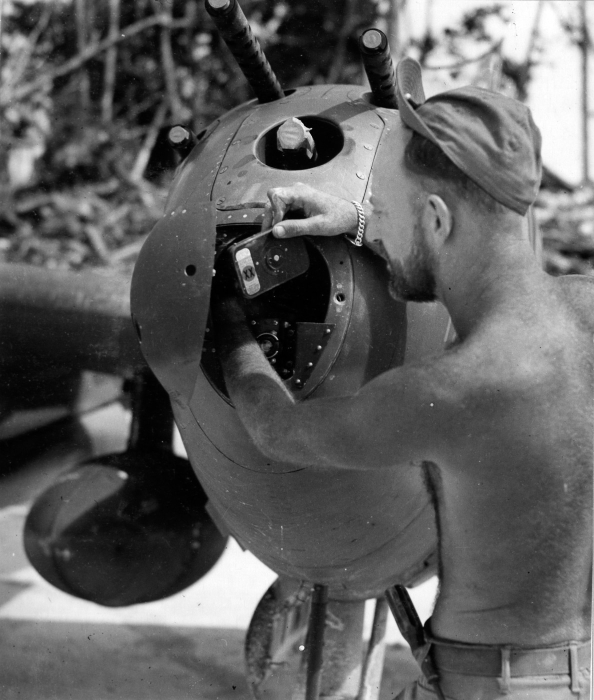Black-and-white close-up photograph of a U.S. Army Air Forces soldier loading film into the gun camera of a P-38 Lightning fighter. The camera is mounted near the aircraft’s nose guns to capture combat footage during aerial engagements. The serviceman carefully threads the film, ensuring it will function during the next mission. Gun cameras were vital for confirming air-to-air victories, reviewing tactics, and providing training material. The image highlights the behind-the-scenes work of ground crews, whose efforts ensured accurate combat records. Such preparations were crucial during missions like Operation Vengeance.