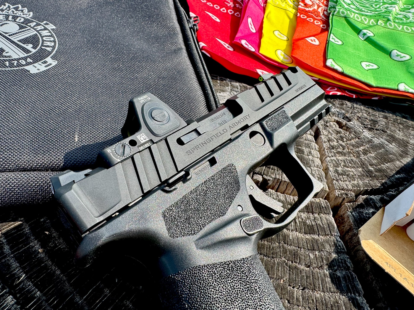 A close-up photograph shows the Trijicon RMR reflex sight with green LED reticle mounted securely on the slide of a Springfield Armory Echelon pistol. The optic sits low thanks to the Echelon’s Variable Interface System, allowing co-witness with standard iron sights. The RMR’s distinctive forged aluminum housing with protective ears is visible, designed to divert impact away from the lens. The green reticle offers quicker visibility compared to red dots, making it easier to pick up against multiple backgrounds. The crisp machining of the Echelon’s slide serrations and optics cut is also clearly visible. This image highlights the optic’s durability, compact design, and integration with a modern duty pistol.