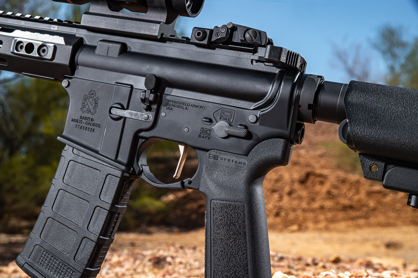 This image shows a sharp, close-up view of the right side of the Springfield Armory SAINT Victor rifle’s lower receiver. The ambidextrous safety selector is prominently displayed just above the trigger guard, featuring clean, government-style low-profile engravings that denote SAFE and FIRE positions. Visible is the forged 7075 T6 aluminum construction, consistent with the model’s overall build quality. The charging handle latch and dust cover are also in view on the upper. The photo captures the refined detailing and tactile controls of the rifle, designed for ergonomic use and quick transitions. Subtle pictograms and clean lines reinforce the visual appeal and intuitive design Springfield has prioritized in the 2025 SAINT Victor update. This close-up speaks to the blend of utility and styling that defines the platform.