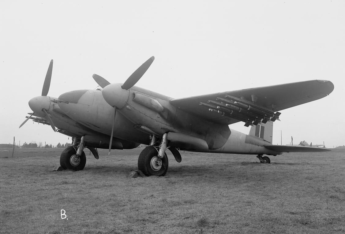 A de Havilland Mosquito FB Mk VI, serial number HX918, photographed on the ground at Hatfield Aerodrome in Hertfordshire, England. The aircraft is seen in side profile, displaying its camouflage paint scheme and fitted underwing rocket projectile rails. Retained by the de Havilland Aircraft Company as a trials machine, this Mosquito was used for weapons development after World War II. The FB Mk VI was the most widely produced fighter-bomber version of the type, equipped with four nose-mounted machine guns, four cannons, and external stores capability. The addition of rockets made it a formidable ground-attack aircraft, effective against shipping, trains, and fortified positions. This image highlights the adaptability of the Mosquito design to carry a wide variety of ordnance. HX918 served as a testbed, bridging wartime combat service with postwar experimentation.