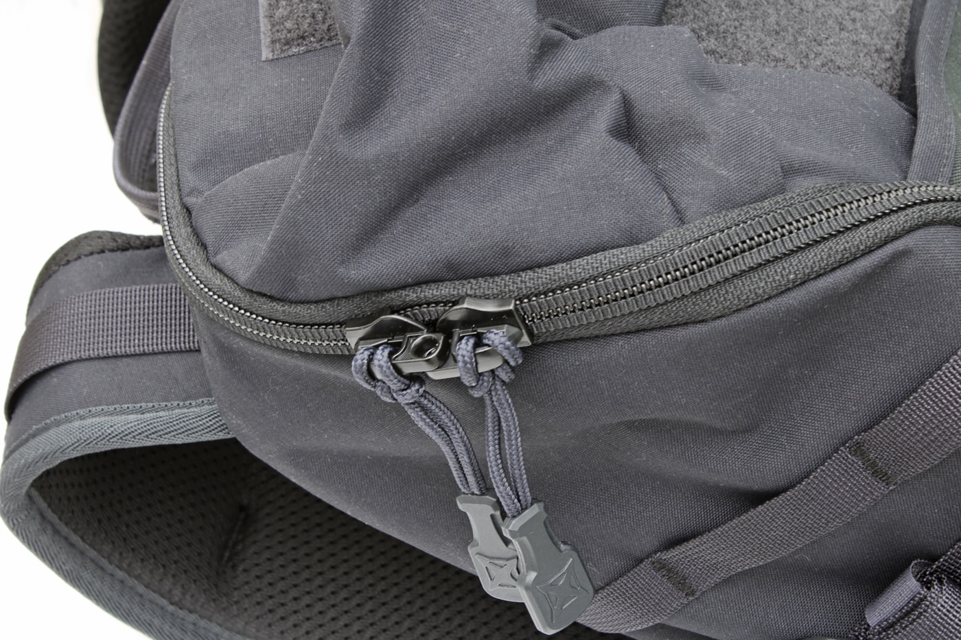 Close-up photo of the Vertx Siege 25L Tactical Backpack’s YKK zippers designed for durability and security. The image shows two zipper pulls with overlapping metal rings that allow a lock to be threaded through them. This feature helps protect valuables or sensitive gear stored inside the main and EDC compartments. YKK zippers are internationally recognized for strength and long life under heavy use. The reinforced zipper tracks resist snagging and wear, even under full load. This detail emphasizes the Siege 25L’s combination of tactical function and everyday reliability. The photo highlights secure compartment access during testing.