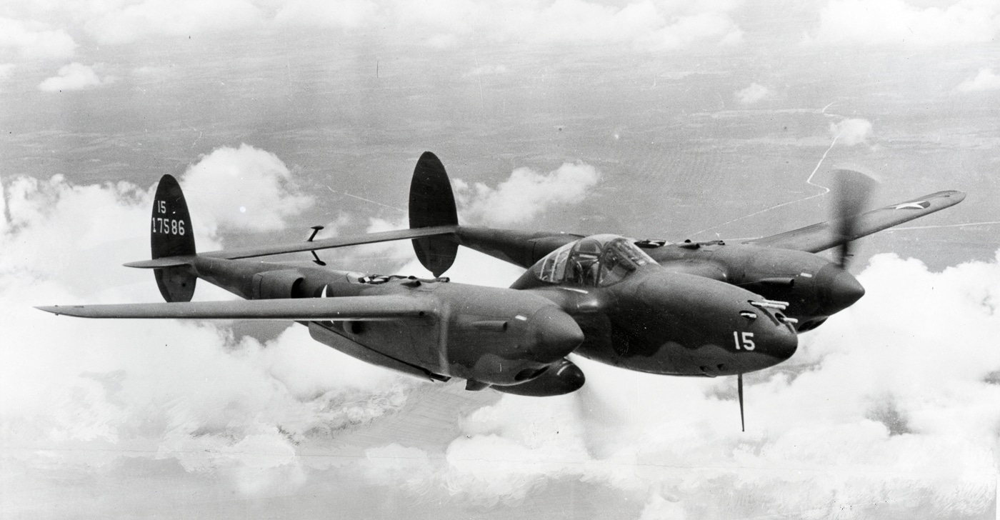 Archival wartime image of the nose and wing of a Lockheed P-38 Lightning, focusing on its weapons and additional fuel capacity. The aircraft’s five-gun armament, with machine guns and a 20mm cannon clustered tightly in the nose, provided devastating forward firepower. An external drop tank is mounted under the wing, a common addition for missions that required extreme range. The design eliminated the need for wing-mounted guns, giving the Lightning superior accuracy at long distances. This loadout was crucial in the Pacific, where fighters often flew hundreds of miles over open water. The image illustrates both the offensive and endurance-oriented features of the aircraft.