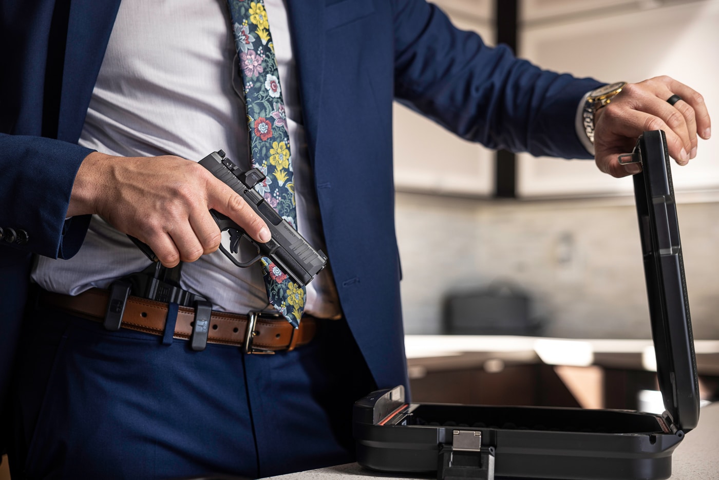 Photo shows a man in a suit carrying a Springfield Armory Hellcat Pro in an inside-the-waistband position, presented as an everyday carry (EDC) self-defense setup. The image captures the pistol partially drawn from under a jacket, highlighting the slim profile and compact grip typical of the Hellcat Pro. The optics-ready slide and short slide length are visible, reinforcing why many consider compact pistols for concealed carry and emergency readiness. This picture is relevant to content about Springfield Armory bug out guns, Hellcat Pro EDC options, and professional concealment strategies. No identifying facial features are shown; the focus is on the pistol and its concealment in formal attire. Lighting and framing emphasize the handgun’s controls and holster position rather than operational detail, keeping the photo suitable for editorial and accessibility uses.