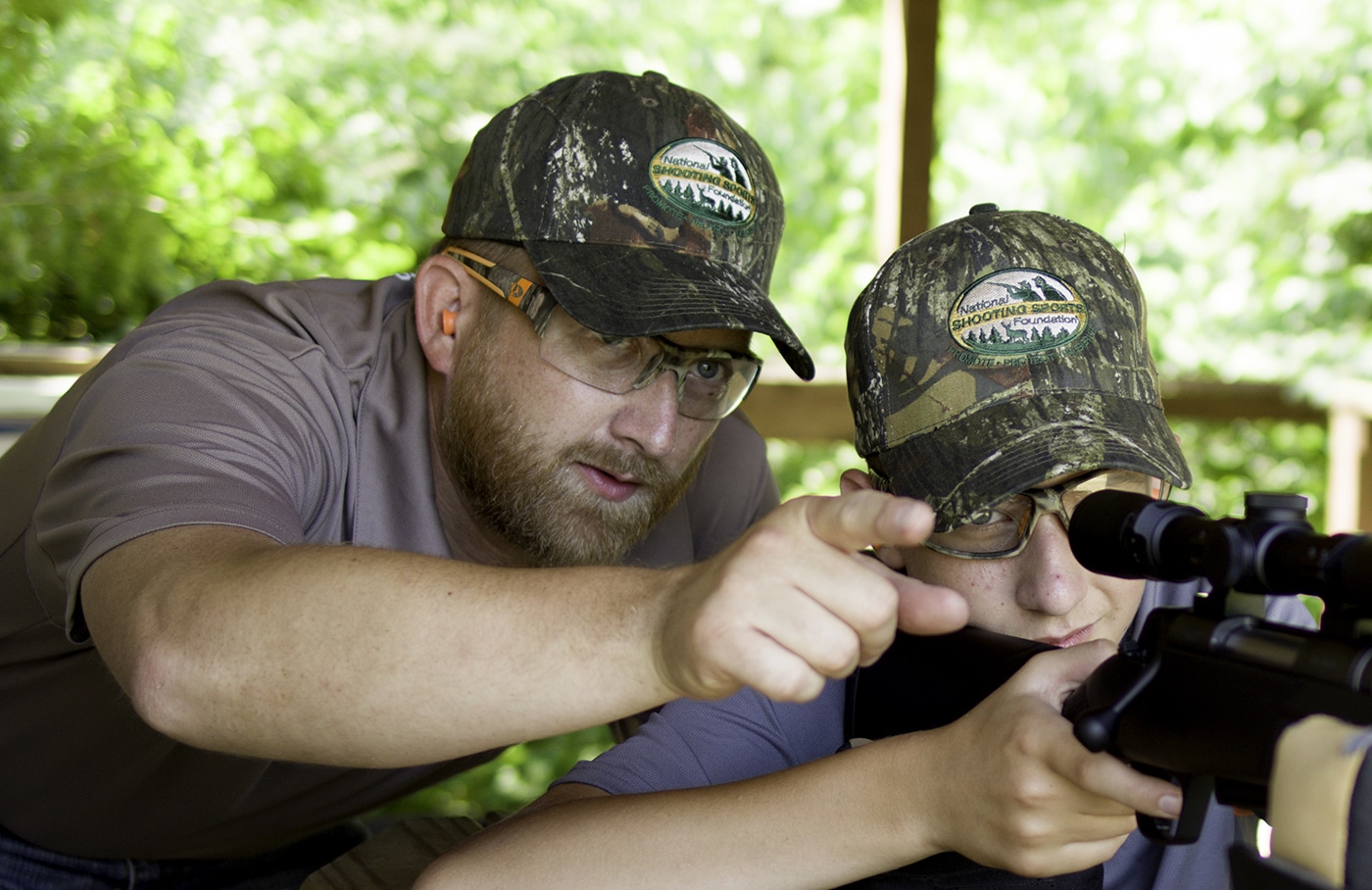 Father teaching son to shoot at gun club showing membership benefits of youth programs and junior shooting instruction. Gun clubs provide junior shooting programs that teach young people firearm safety marksmanship fundamentals and shooting skills under certified instructors. Joining shooting clubs offers families access to youth rifle teams pistol programs and junior competitions that develop shooting abilities in children. Firearms club membership includes junior programs where young shooters learn gun safety proper shooting techniques and competitive skills with provided equipment. Shooting range club members benefit from youth instruction programs that teach children marksmanship fundamentals firearm safety and shooting sports without families purchasing all guns ammunition and gear upfront.