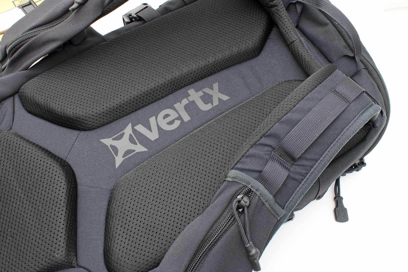 Close-up photo of the Vertx Siege 25L Tactical Backpack showing padded shoulder straps and a ventilated mesh back panel. The padding is thick enough to provide comfort during long periods of wear but not overly bulky. Adjustable straps with quick-release buckles are visible, allowing users to customize fit. The mesh fabric increases airflow to reduce heat buildup during extended use. This design makes the backpack suitable for hiking, range days, or daily commuting. Reinforced stitching ensures durability under heavy loads. The photo highlights the comfort-focused construction of the pack.