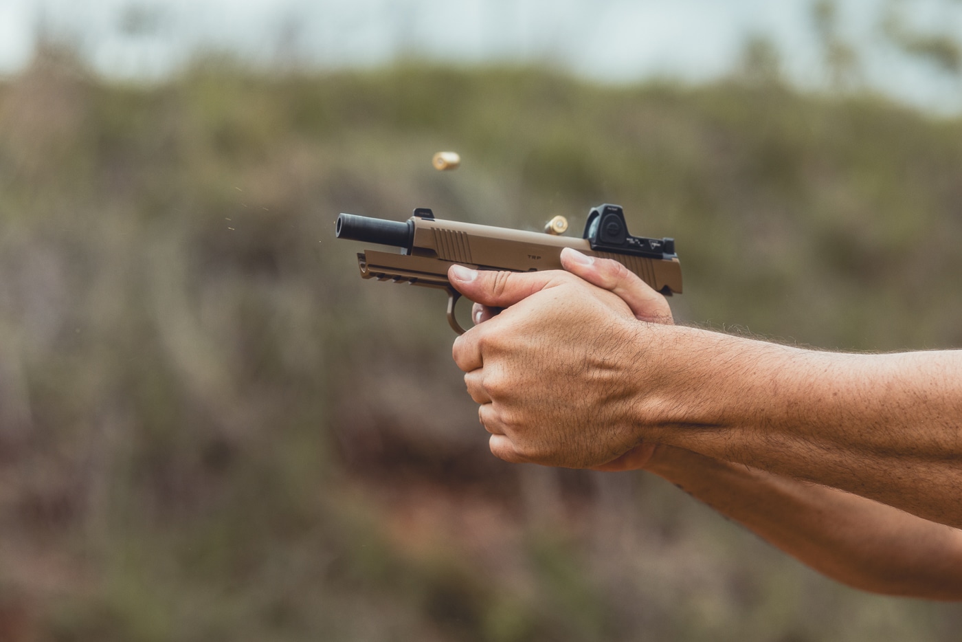 A Springfield Armory TRP 1911 AOS with a red dot sight is shown mid-sequence during rapid fire drills. The pistol’s optic is mounted directly into the slide cut, emphasizing the Agency Optic System’s secure fit. The shooter is in a live-fire stance with the pistol cycling, capturing the motion and energy of rapid shooting. The red dot sight provides a single aiming reference, aiding speed and accuracy. Key pistol features such as G10 grips, skeletonized trigger, and forward serrations can be seen. The photo demonstrates how the TRP AOS blends traditional handling with the advantages of modern optics under demanding conditions.