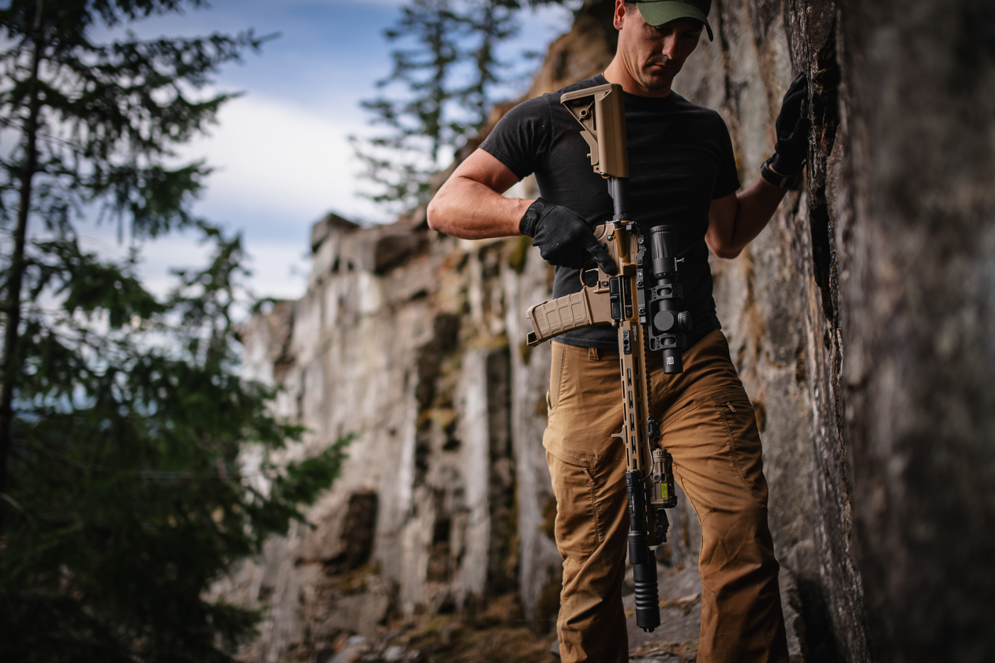 The image shows a shooter navigating through wooded terrain while carrying a Springfield Armory SAINT Victor rifle chambered in .308 Winchester. The shooter is holding the rifle in a ready position, moving carefully through trees and natural cover. This rifle features a free-float aluminum handguard with M-Lok slots and a full-length Picatinny top rail for optics or backup sights. The configuration includes B5 Systems furniture, with an Enhanced SOPMOD stock for stable shoulder placement and a Type 23 P-Grip for improved control. A four-prong flash hider can be seen at the muzzle, consistent with Springfield’s updated Victor design. The rifle’s larger .308 Winchester chambering makes it well-suited for long-range accuracy and higher energy on target. The photo highlights real-world handling, showing how the SAINT Victor is designed to function effectively in field conditions.