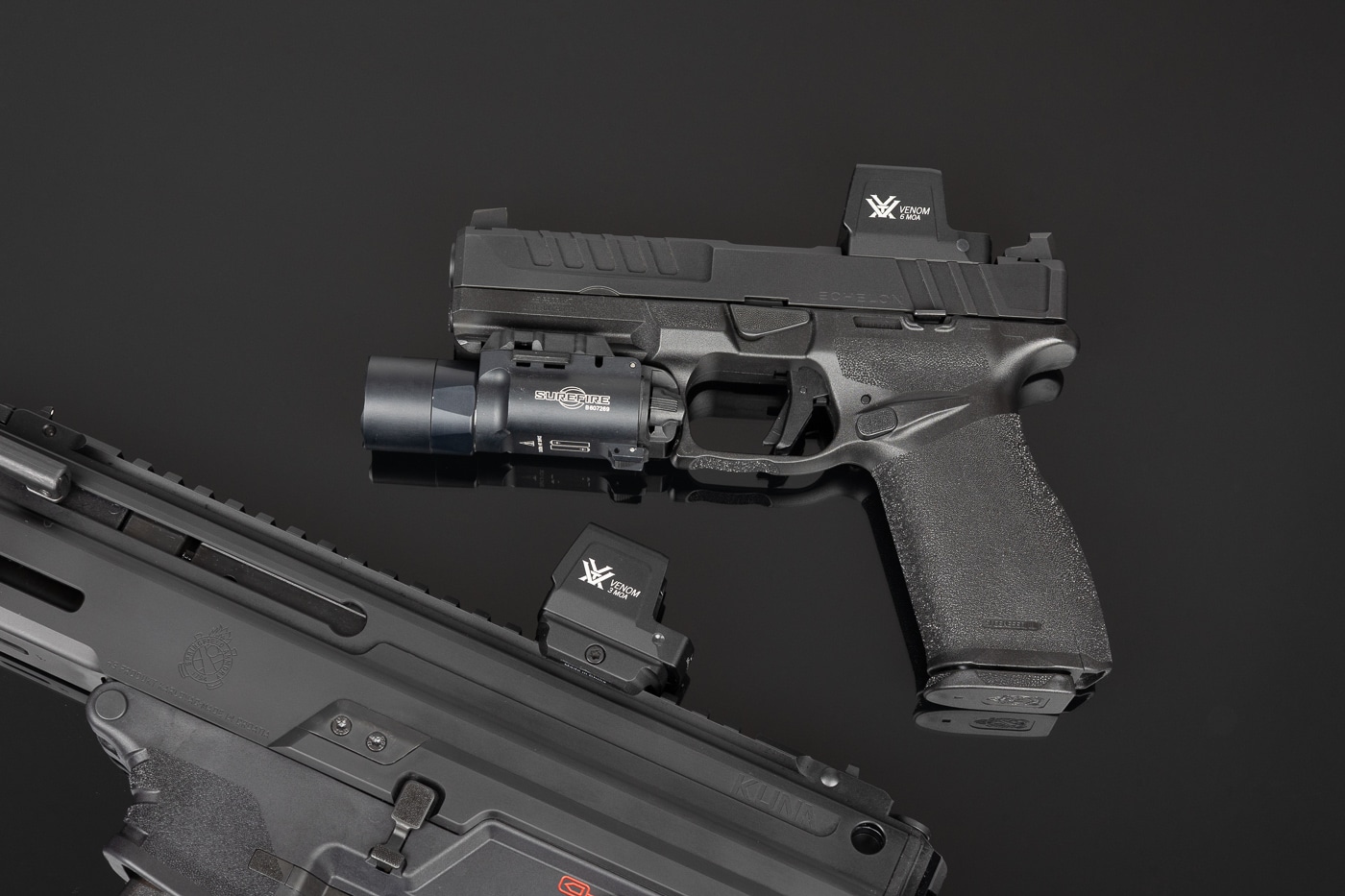 Photo of two Springfield Armory pistols placed side-by-side, each fitted with a Vortex Venom Enclosed red dot sight  —  the left pistol has the 3 MOA model and the right sports the 6 MOA. The image clearly shows the difference in dot size when viewed through the optic windows, with the 3 MOA offering a smaller aiming point and the 6 MOA providing a larger, faster-to-acquire reticle. Both optics feature the closed-emitter housing that protects the dot from dust, sweat, and range debris. The mounts use the DeltaPoint Pro-compatible footprint and sit low on the slides, allowing partial co-witness with factory iron sights. Side-loading CR2032 battery trays are visible on both units, illustrating battery changes without removing the optic. This visual supports the Vortex Venom Enclosed red dot sight review by showing practical hardware differences for carry, duty, and precision applications.
