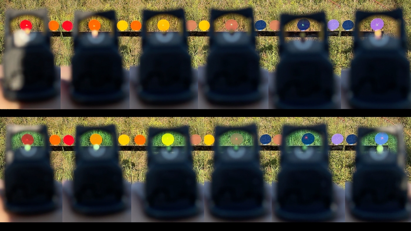 The image shows a comparison of the Trijicon RMR red and green LED reticles as viewed through the optic’s lens and projected onto targets. On the left, the red dot appears against the background, while on the right, the green dot is visible with more contrast and brightness. The green reticle aligns with the human eye’s peak sensitivity, making it easier to detect in challenging light or busy backgrounds. Both reticles remain crisp and functional, offering fast target acquisition. The lens tint differences between red and green models are visible, with one showing a slight color shift. This image illustrates how reticle color choice impacts visibility and shooting performance.