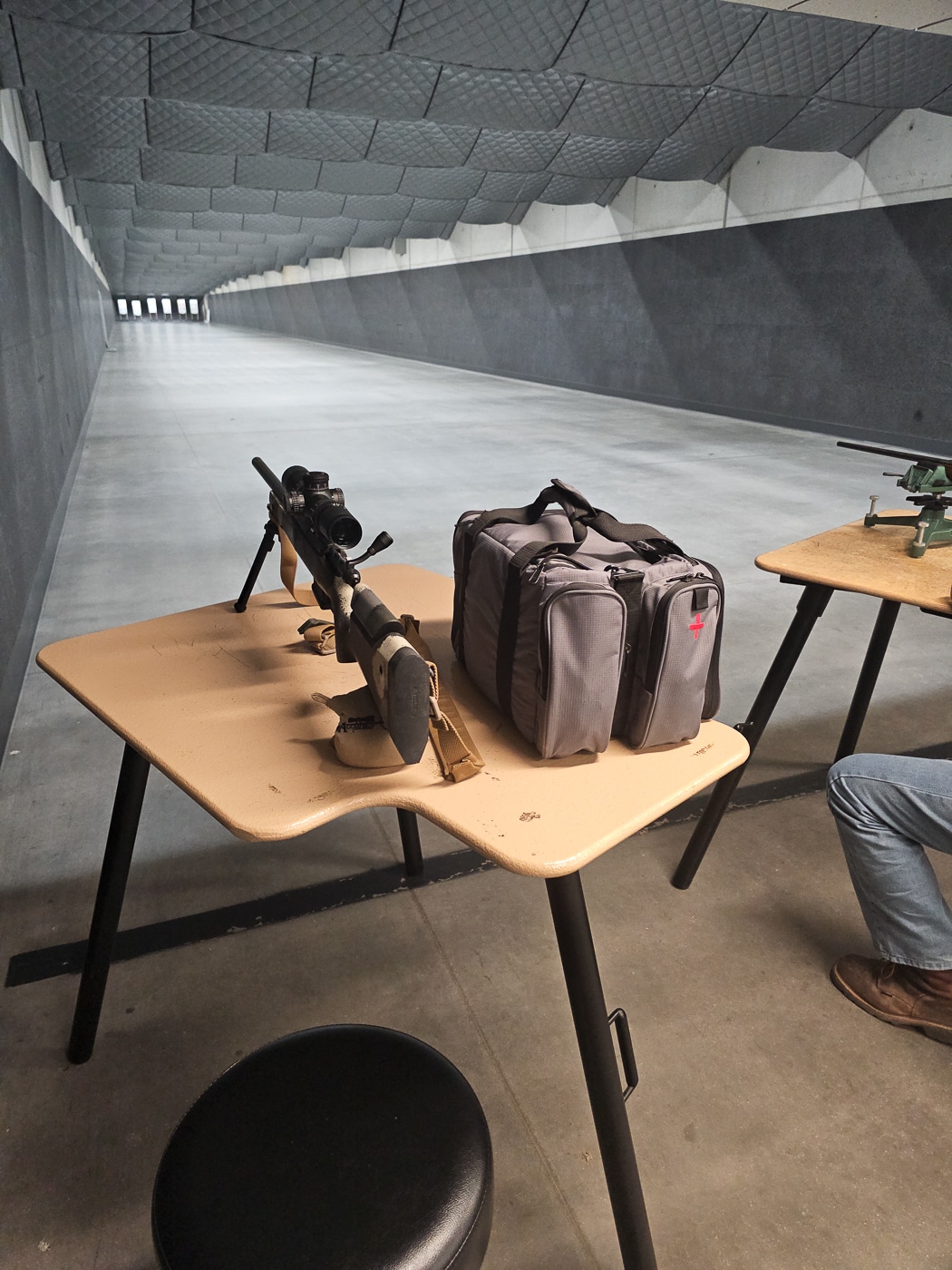 Wide view of the 100-yard indoor range used during the Vortex Optics Hunter Marksmanship Course, featuring individual shooting lanes with target carriers and bright overhead lighting. Shooters are positioned at benches with rifles supported by bipods or rests while instructors observe from behind. The environment is clean and quiet, allowing participants to focus on shot consistency and scope adjustments. Paper targets are visible downrange at the full 100-yard mark. This setup provides a wind-free space to confirm zero, test ammunition groupings, and ensure optic alignment. The image reflects a structured part of the course where data gathering and precision shooting are the primary focus.