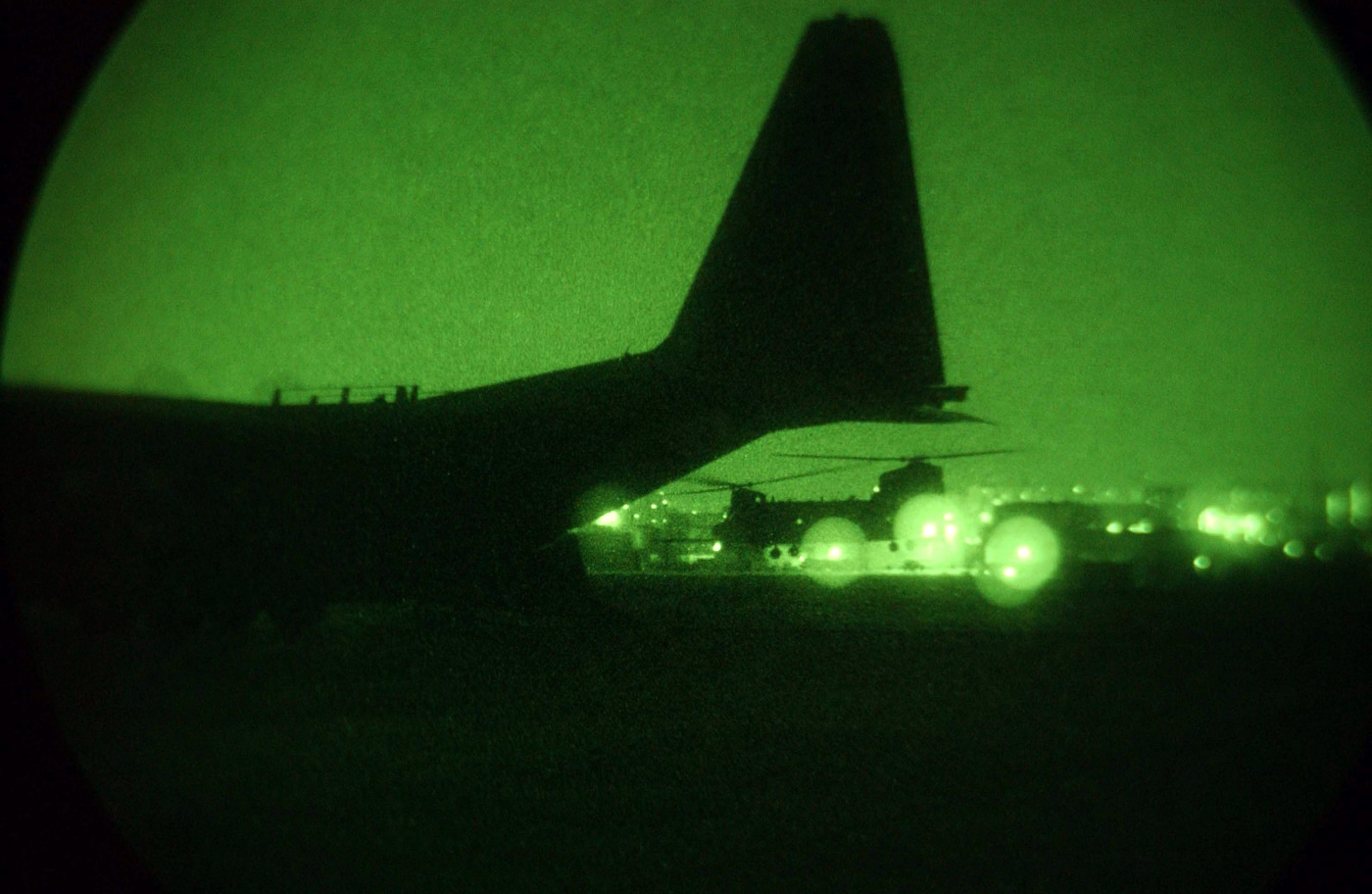 In this nighttime photo, a MH-47G Chinook from the 160th SOAR is shown landing on the runway at Tague Air Base, Korea. The helicopter is equipped with features for special operations, such as refueling probes and additional sensors, visible in the low light. The ground is illuminated by airport lights, casting shadows and reflecting off the aircraft. Crew members or support personnel may be waiting nearby, wearing reflective vests or carrying flashlights. The night sky and distant airbase buildings form the backdrop, with the Chinook as the main focus. The image emphasizes the Night Stalkers’ capability to operate and land in total darkness, often in challenging or unfamiliar locations. The scenario is typical of special operations aviation, where rapid, precise movement is critical. The photo supports the article’s coverage of the regiment’s night mission expertise.