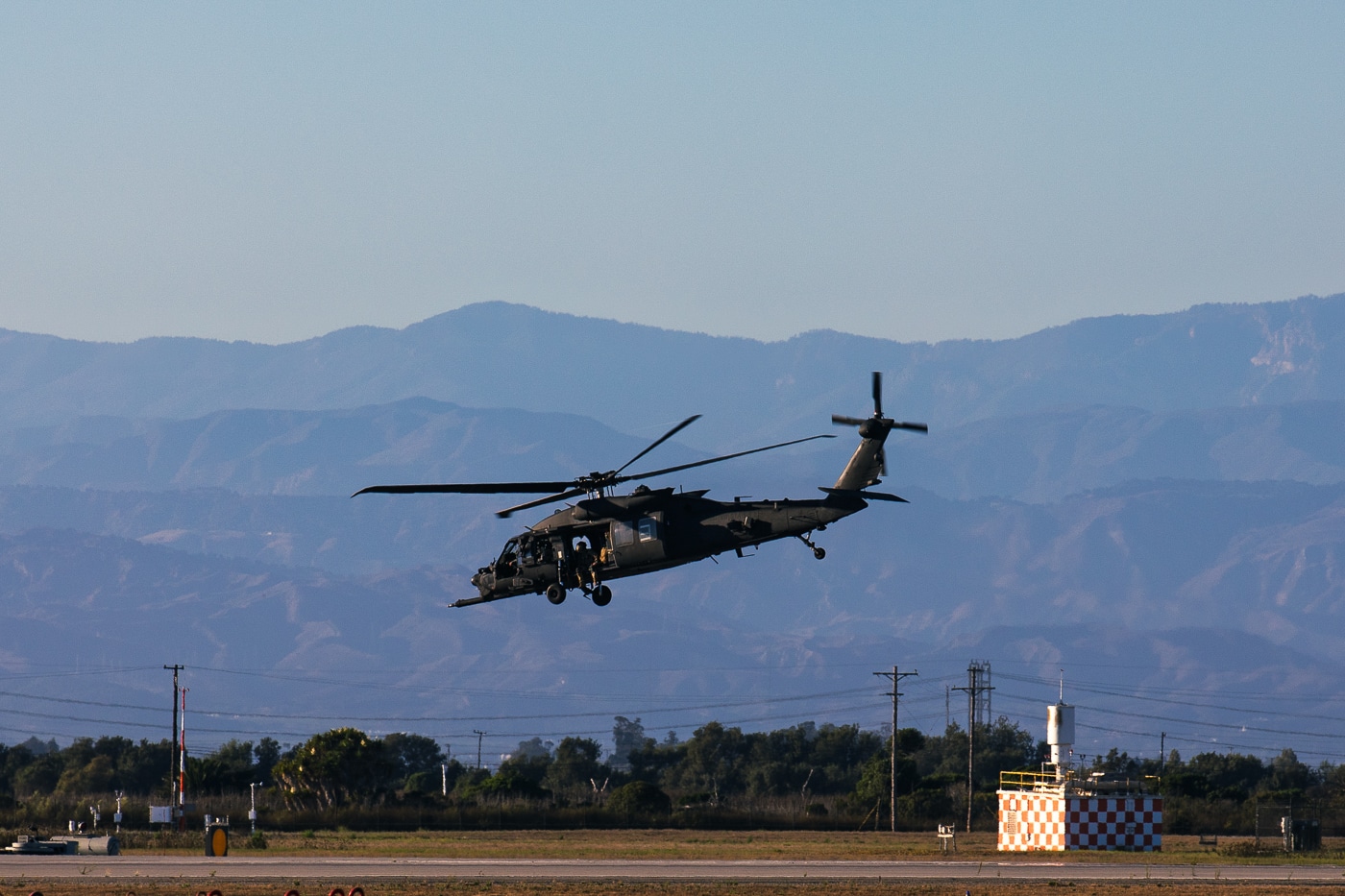 The photo shows a 160th Special Operations Aviation Regiment (Airborne) MH-60M Black Hawk helicopter taking off from Naval Air Station Point Mugu during a training event. The helicopter’s rotors are spinning, and dust or debris may be visible beneath it as it lifts from the tarmac. The background includes elements typical of a military airfield, such as runways, hangars, or other aircraft. The MH-60M is equipped with features specific to special operations, such as external fuel tanks or advanced avionics. This training exercise is part of routine operations that keep Night Stalkers pilots and crew ready for a wide range of missions. The image highlights the emphasis on flight proficiency and operational readiness within the 160th SOAR. It represents the regiment’s continuous commitment to excellence in Army aviation.