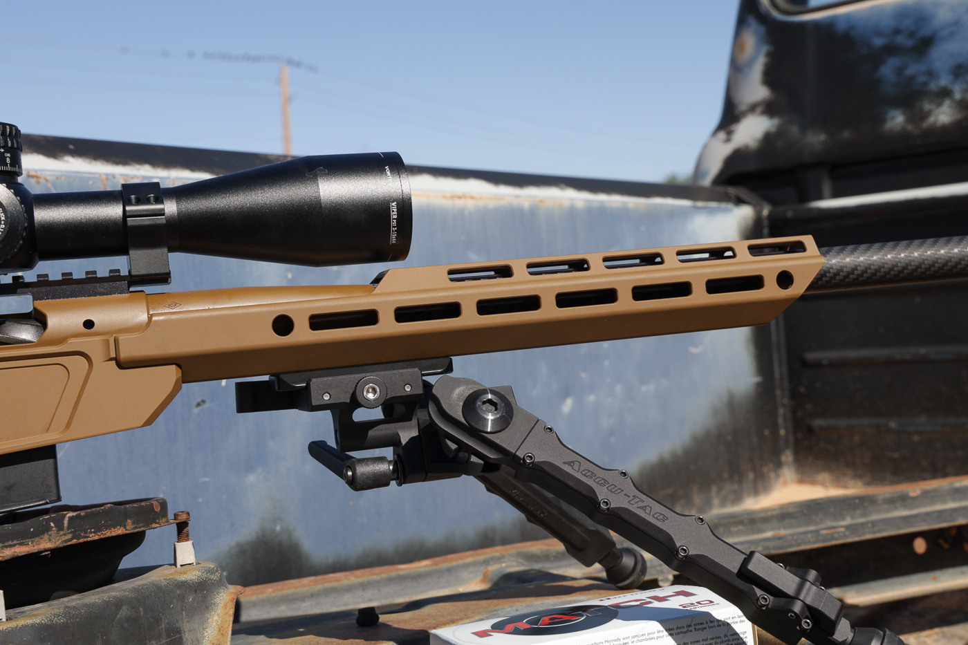 Accutac WB-04 bipod attached to M-Lok rail system on Springfield Model 2020 Heatseeker precision chassis rifle showing wide stance leg configuration. The black anodized aluminum bipod legs extend from mounting point on Sharps Brothers chassis forend providing adjustable height for prone shooting positions. Bipod features robust construction designed to handle loading force when shooter applies pressure into rifle for recoil management. The wider leg spread compared to standard bipods offers increased stability during firing especially for taller shooters. Carbon fiber barrel visible above bipod mount with Coyote Brown Cerakote chassis providing color contrast. This bipod choice proved effective during accuracy testing where rifle produced sub-quarter MOA groups with factory match ammunition. Mounting system integrates cleanly with chassis rail without adding excessive weight to front end.