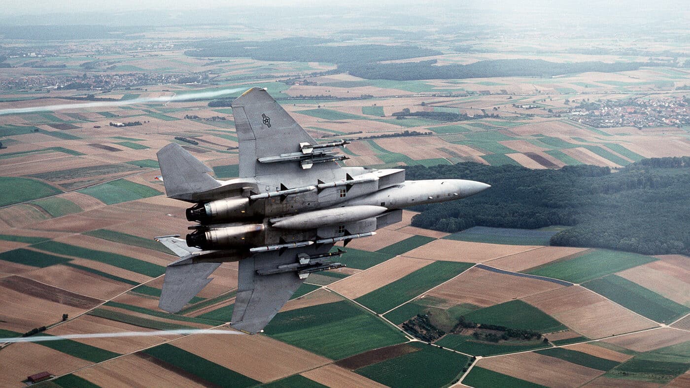 An F-15C Eagle aircraft from the U.S. Air Force’s 36th Tactical Fighter Wing banks left shortly after takeoff during deployment to Saudi Arabia for Operation Desert Shield in 1990. The air-to-air photo shows the fighter fully armed with AIM-7 Sparrow radar-guided missiles under its fuselage and AIM-9 Sidewinder heat-seeking missiles on its wing pylons. The aircraft’s gray camouflage scheme and twin vertical stabilizers are clearly visible. Operation Desert Shield marked the buildup of coalition forces in response to Iraq’s invasion of Kuwait. This image captures the readiness and strength of American air power heading to the Persian Gulf. The F-15C Eagle’s unmatched combat performance made it a critical component of the U.S. air campaign.