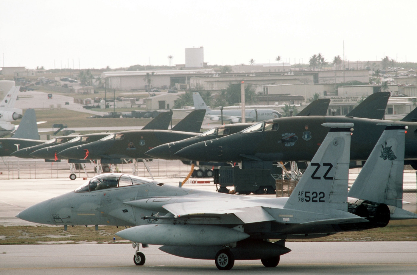 An 18th Tactical Fighter Wing F-15C Eagle is seen taxiing past a row of B-1B Lancer bombers belonging to the 28th Bombardment Wing during Exercise Giant Warrior ’89 at Andersen Air Base, Guam. The photo captures the contrast between the sleek single-seat fighter and the large four-engine bombers lined up on the tarmac. The F-15C’s twin tails and gray camouflage are clearly visible as ground crew members observe nearby. Exercise Giant Warrior tested the ability of tactical and strategic aircraft to operate together in joint strike and air defense missions. The B-1Bs represented America’s long-range bomber force, while the F-15Cs provided air superiority cover. This image highlights the scale and coordination of U.S. Air Force operations in the Pacific during the late Cold War. The scene conveys both readiness and power projection capability.