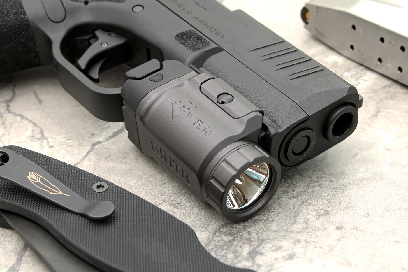 The photo introduces the GRITR TL1c as the centerpiece of the review, with the light mounted to a typical concealed carry handgun. The image is neutral and professional, suitable for use as a lead image in a gear review article. Readers can see the overall construction, color, and mounting interface of the weapon light. This photo is broad enough to represent discussions of features, operation, and real-world use that follow in the article body. The product’s size and finish are clear, with a subtle focus on how it integrates with everyday carry pistols. The composition is simple and draws attention to the product, making it useful for an overview or summary section. Keywords include GRITR weapon light, pistol accessory review, and tactical lighting.