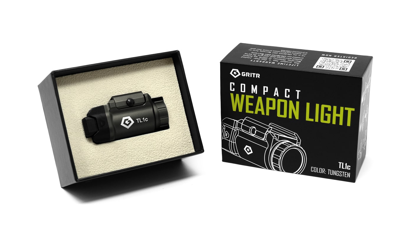 Photo of the GRITR TL1c Compact Weapon Light displayed inside its original retail box, with the light and included accessories neatly arranged in their designated slots. The packaging contains the light, a CR123A battery, multiple rail spacers, an instruction manual, and possibly a tool for installation. The interior is organized to prevent damage during shipping and provides a clear overview of what the buyer receives. The box design is straightforward and professional, reflecting the brand’s no-nonsense attitude.