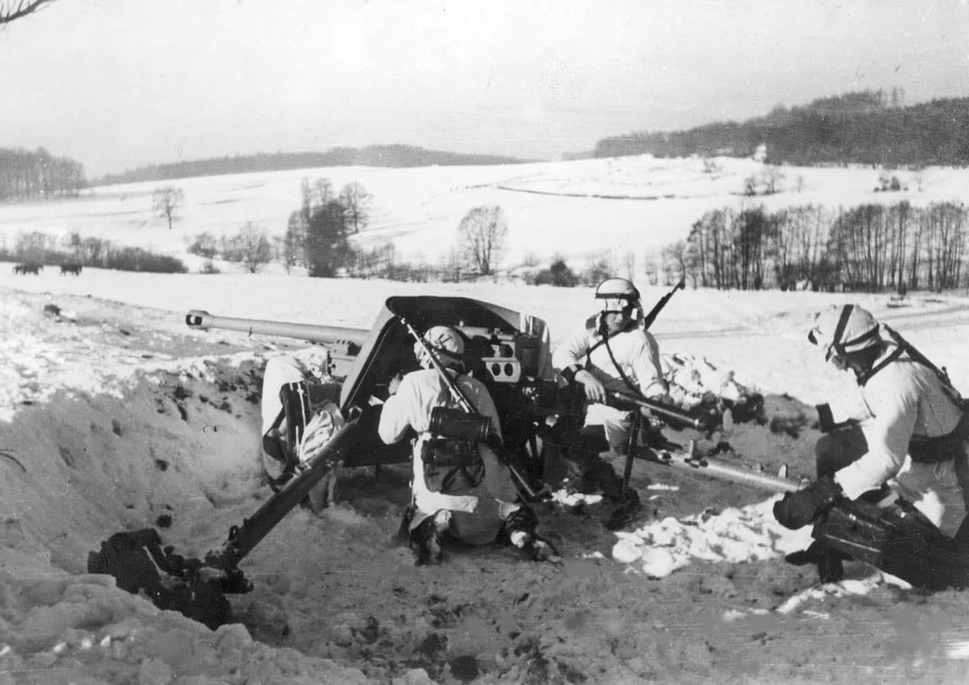 A World War II photograph shows a 50 mm Pak 38 anti-tank gun in a dug-in position on the Eastern Front. Soldiers of the 14th Waffen SS Grenadier Division “Galizien” are visible manning the emplacement. The gun, introduced in 1940, was capable of penetrating medium armor at short to medium ranges but struggled against newer Soviet tanks like the T-34. The crew appears focused on operating the weapon, with one soldier at the breech and others supporting. The emplacement is reinforced with earth and brush for camouflage and protection. This photo illustrates the continued use of Pak 38s even after more powerful weapons became necessary.