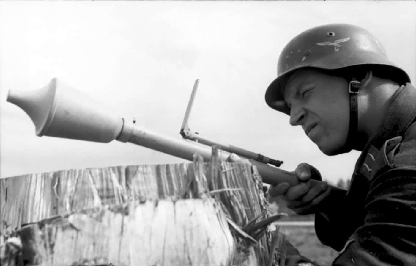 A German Luftwaffe private is shown during training with a Panzerfaust on the Eastern Front. The soldier holds the single-use anti-tank launcher, preparing to aim and fire. The Panzerfaust was designed for close-range attacks, with different models offering effective ranges from 30 to 100 meters. Its shaped-charge warhead could penetrate the armor of Soviet tanks such as the T-34. The training exercise highlights the emphasis placed on familiarizing even non-army personnel, like Luftwaffe ground troops, with anti-tank tactics. The image demonstrates the simplicity and portability that made the Panzerfaust widely issued in the last years of the war.