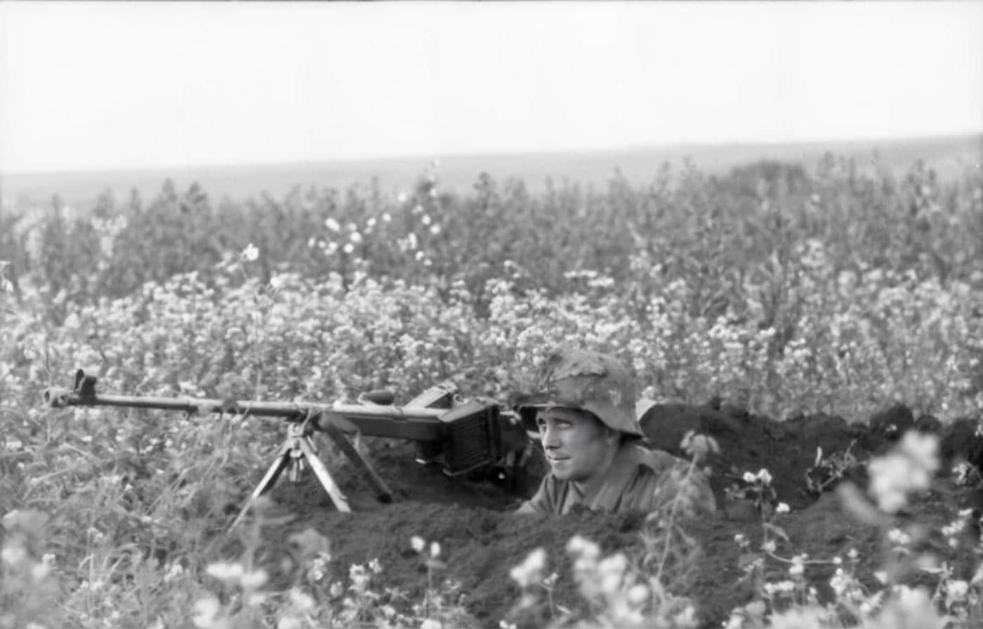 A German soldier crouches in a foxhole on the Eastern Front armed with a Panzerbüchse 39 anti-tank rifle. The soldier positions the long, heavy rifle across the rim of the position as if preparing to fire. The PzB 39 fired a high-velocity 7.92 mm round designed to penetrate thin armor. By 1941, however, the weapon was largely ineffective against Soviet T-34s and KV tanks. Its continued use was mostly limited to engaging light vehicles and unarmored targets. This image demonstrates how outdated equipment remained in use, particularly in defensive situations.