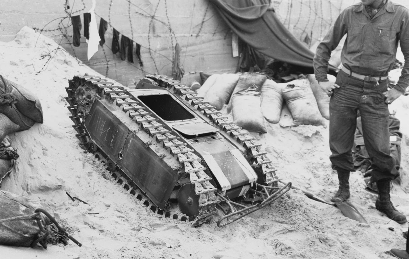 A German Goliath anti-tank weapon is shown, a small tracked demolition vehicle designed during World War II. The machine, officially called the Leichter Ladungsträger Goliath, carried a large explosive charge and was controlled by a cable. It was intended to drive under enemy tanks or fortifications before detonation. Despite its advanced concept, the Goliath had limited speed and armor protection, making it vulnerable on the battlefield. Allied troops often destroyed them before they could reach their targets. The photo emphasizes the compact size of the vehicle compared to traditional tanks.