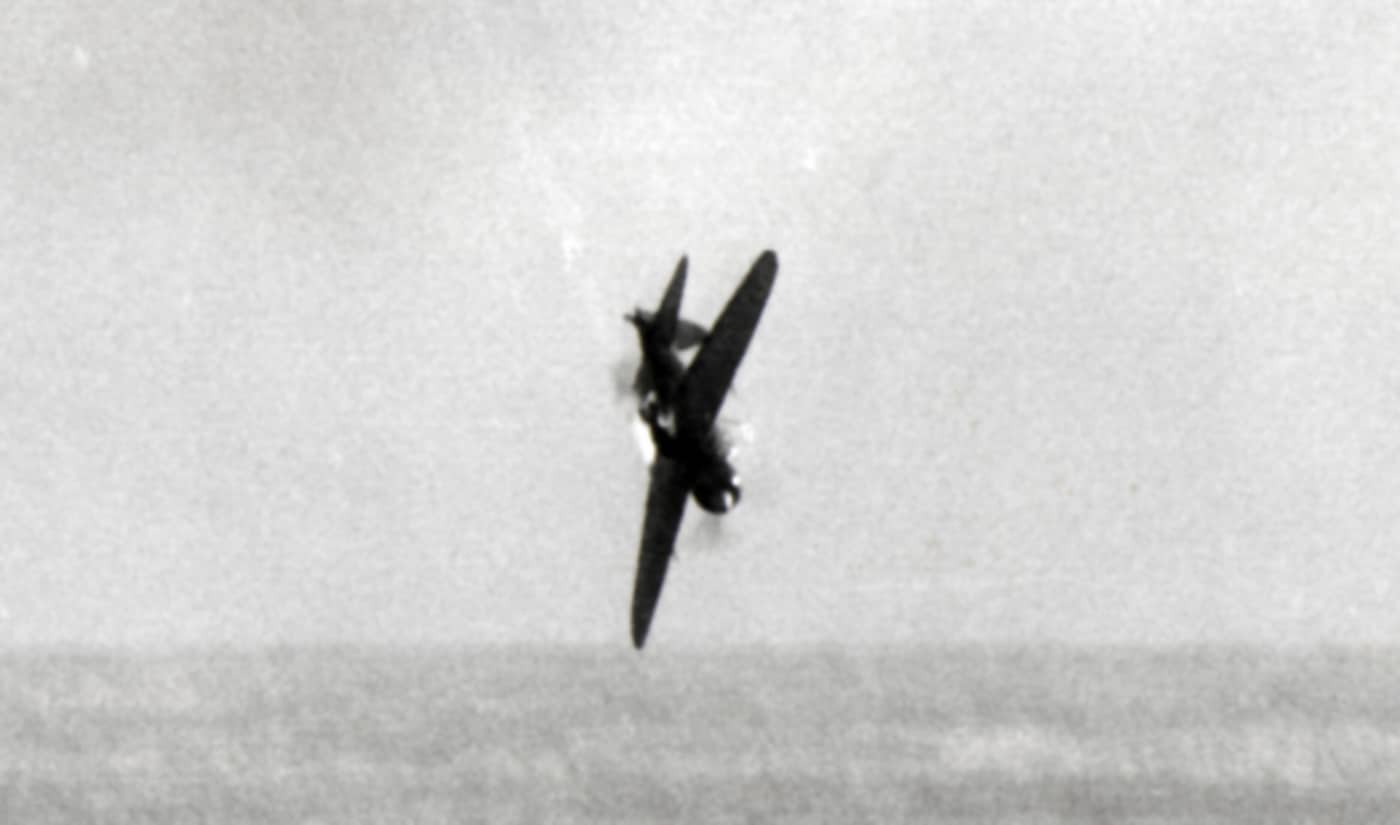 A wartime photo captures a Japanese Yokosuka D4Y “Suisei” dive bomber engulfed in flames as it crashes toward the ocean in 1945. Thick black smoke pours from its engine and fuselage, forming a long trail against the sky. The aircraft’s nose is sharply angled downward, showing it’s moments from impact. Anti-aircraft bursts and debris can be seen in the background, indicating it was hit during an attempted kamikaze attack. The scene highlights both the desperation of Japan’s final air missions and the growing accuracy of U.S. Navy gunners. The image represents the broader story of Japanese Kamikazes in World War II and the destructive air battles near Okinawa and the Philippines.