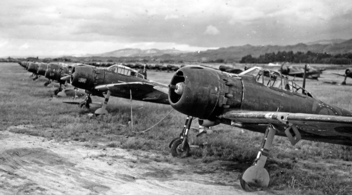 A postwar photo showing multiple Japanese Mitsubishi A6M “Zeke” (Zero) fighter planes parked in neat rows on an airfield, each with its propeller removed. The aircraft appear weathered and abandoned, their engines exposed. U.S. military personnel can be seen inspecting or walking among them, likely during the early stages of occupation in 1945. The photo symbolizes the end of Japan’s air war and the disarming of kamikaze-capable aircraft. Without propellers or armament, these planes could no longer be used for suicide missions. The image illustrates the transition from combat to surrender, marking the final phase of Japanese Kamikazes in World War II.