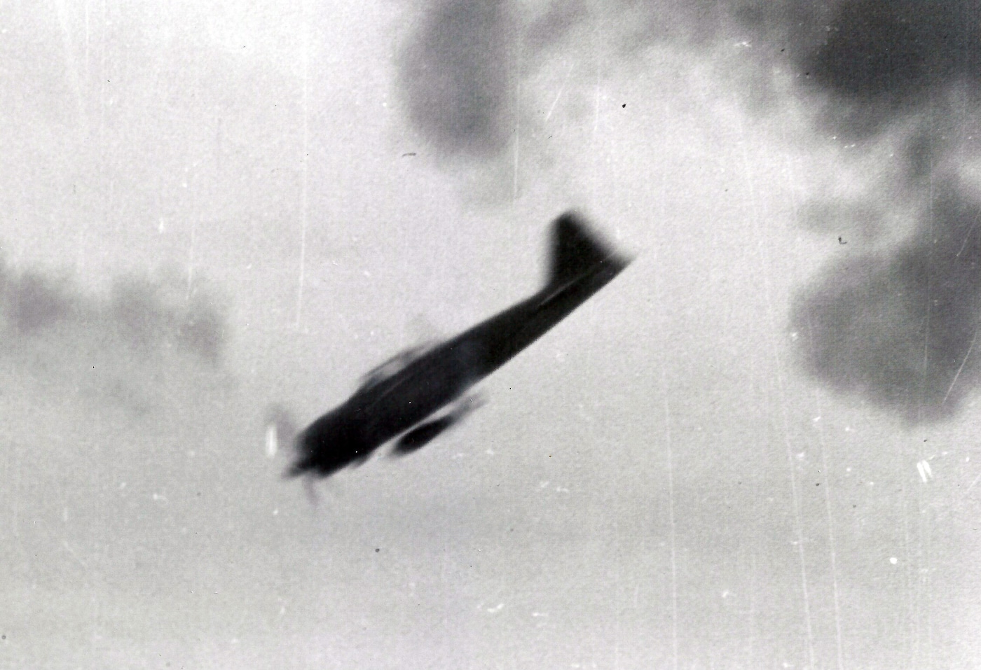 A wartime photo capturing a Japanese Mitsubishi A6M2 “Zeke” fighter diving steeply toward a U.S. Navy ship during the Marianas campaign of World War II. The aircraft is nose-down, trailing faint smoke, its wings glinting in the sunlight. Below, a naval vessel can be seen surrounded by the splashes of near-miss anti-aircraft fire. The photo conveys the terrifying speed and precision of a kamikaze death dive. The pilot’s determination contrasts sharply with the defensive fire erupting from the ship’s guns. This image illustrates the deadly moment before impact — one of many scenes repeated across the Pacific in 1944–45.