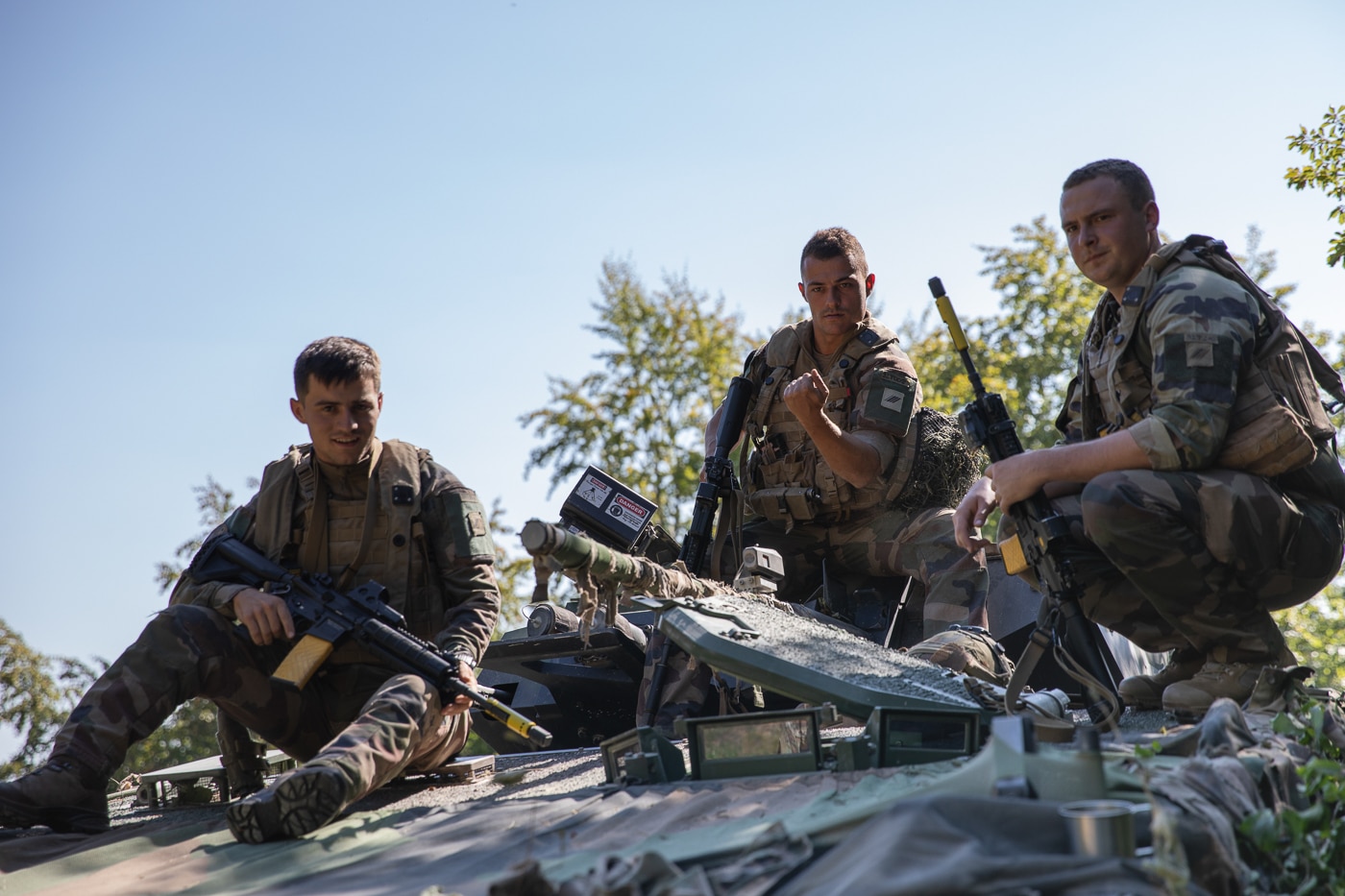 The image shows the three-man crew of a French Leclerc main battle tank taking a break during NATO training in 2023. The soldiers are in standard combat uniforms and appear relaxed between drills. Unlike most NATO tanks, which require four crew members, the Leclerc’s autoloader system reduces the crew to a commander, gunner, and driver. The photo emphasizes the human element of operating the tank, showing the men who work inside its compact interior. Training exercises like this highlight both the technical and personal demands of armored warfare. The image captures a candid moment of rest in the midst of intensive military training.