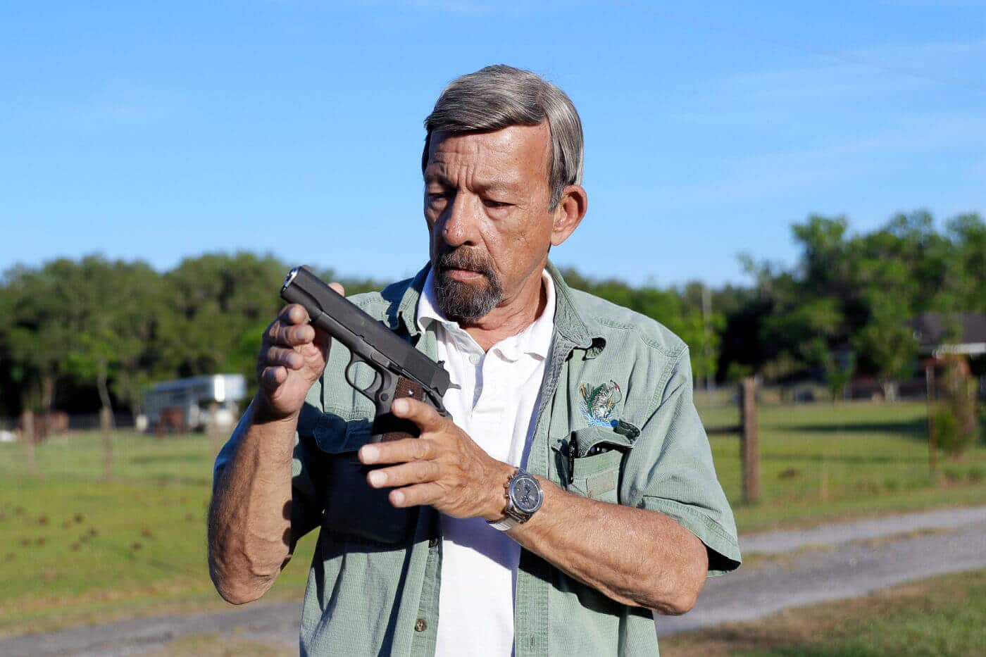 Massad Ayoob holding a standard configuration 1911 pistol demonstrating the practical defensive handgun he recommends over expensive custom variants. His grip shows the natural pointability and slim profile that makes basic models surprisingly concealable for full-size pistols. The plain jane .45 automatic in his hands lacks optical sights, extended dust covers, or competition-grade trigger work. Ayoob's decades of experience validate choosing affordable reliability over costly enhancements for self-defense purposes. Standard 1911 models fed dependably and stopped threats effectively throughout military and law enforcement history. The fundamental design by John Browning provides adequate power, low bore axis for rapid fire, and redundant safety features without modification. Basic versions like the Springfield Armory Mil-Spec cost around $725 compared to $3,000 for fully customized guns.