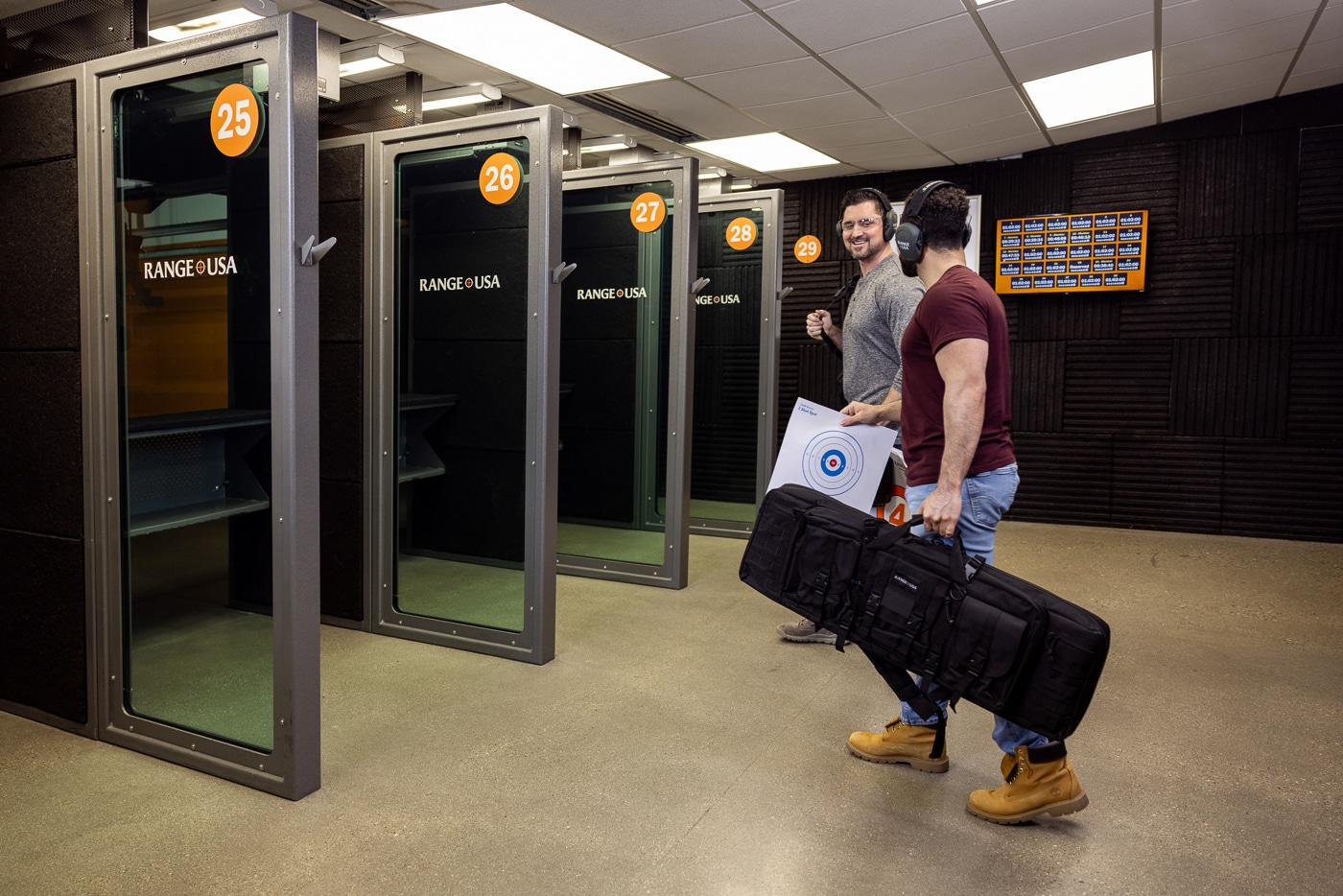 Image of several Range USA customers preparing to shoot inside a brightly lit indoor shooting range. Participants are wearing ear and eye protection while setting up firearms and targets at individual lanes. Each booth is separated by safety barriers and equipped with benches for gear. The range design is modern and organized, emphasizing visibility, ventilation, and comfort. Staff members may be visible in the background overseeing operations. The photo reflects Range USA’s commitment to maintaining safe, professional, and accessible shooting environments. It captures the brand’s focus on community and hands-on training experiences.