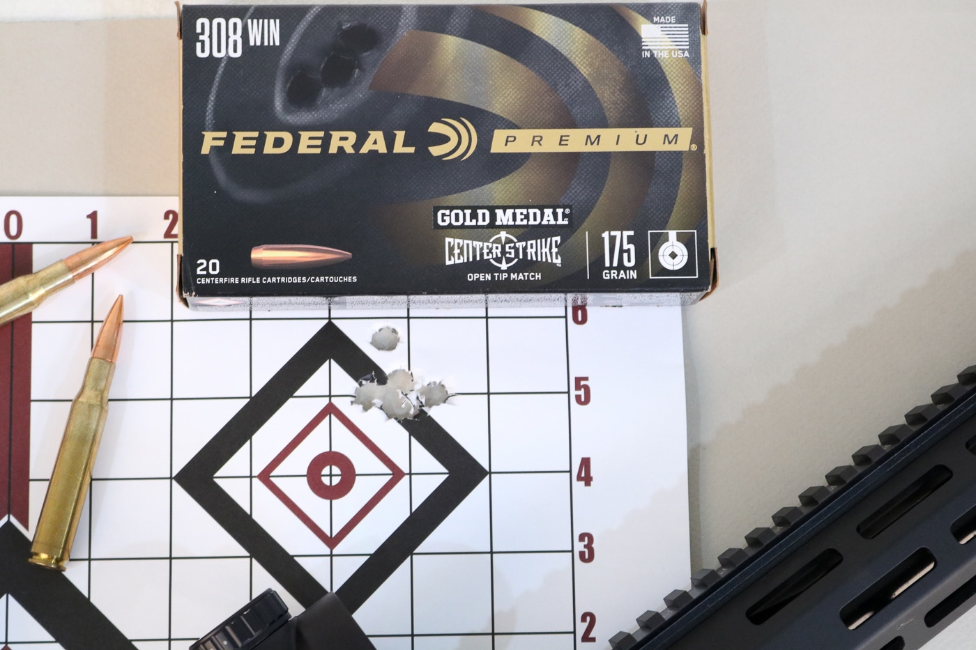 A Springfield Armory AR-10 rifle is shown beside a paper target with small, consistent shot groups produced using Federal Gold Medal ammunition. The rifle rests on a support or bench, fitted with an optic for precision shooting. The target displays several tight clusters of bullet holes, demonstrating the .308 platform’s potential for high accuracy. The Federal Gold Medal ammunition box is visible, identifying the match-grade load used in testing. The lighting emphasizes clean, precise impacts and the rifle’s modern tactical build. This image visually represents controlled range performance rather than casual shooting. It reinforces how the AR-10, when paired with quality ammunition, can deliver sub-MOA accuracy and consistency.