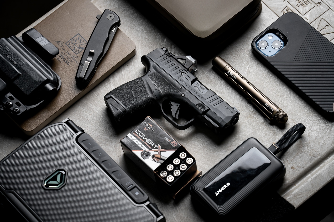 A top-down photo shows a Springfield Hellcat 380 ACP pistol arranged next to a spare magazine, loose rounds, and everyday carry items such as a wallet and smartphone. The micro-compact Hellcat .380 is positioned so the short slide, textured grip, and U-Dot sight are visible. Ammunition is displayed nearby to indicate caliber and capacity context for the review. Everyday items like keys and a slim wallet convey how the pistol fits into a typical EDC setup for concealed carry. The image emphasizes concealability and practicality rather than tactical display. Lighting is even, with focus on the pistol’s profile to make details clear for readers. This picture supports article sections about packing, daily carry choices, and how the Springfield Hellcat 380 ACP integrates into routine life.
