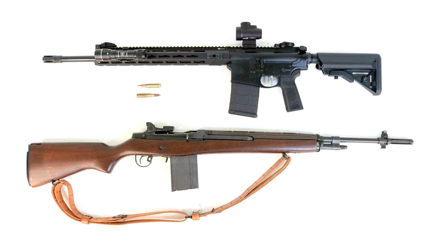 An overhead photo displays the Springfield Armory M1A and the SAINT Victor AR-10 placed side by side for visual comparison. The M1A features a wood stock with a timeless military profile, while the AR-10 uses a modular black aluminum and polymer build. This image introduces the article comparing both rifles’ design philosophies and roles. The setup highlights how each rifle approaches the same .308 chambering from completely different perspectives. Clean lighting draws out surface textures and details on both firearms. The contrast of materials — wood versus metal — underscores the old-meets-new theme of the piece. The photo sets the tone for the reader to explore performance, ergonomics, and legacy differences.
