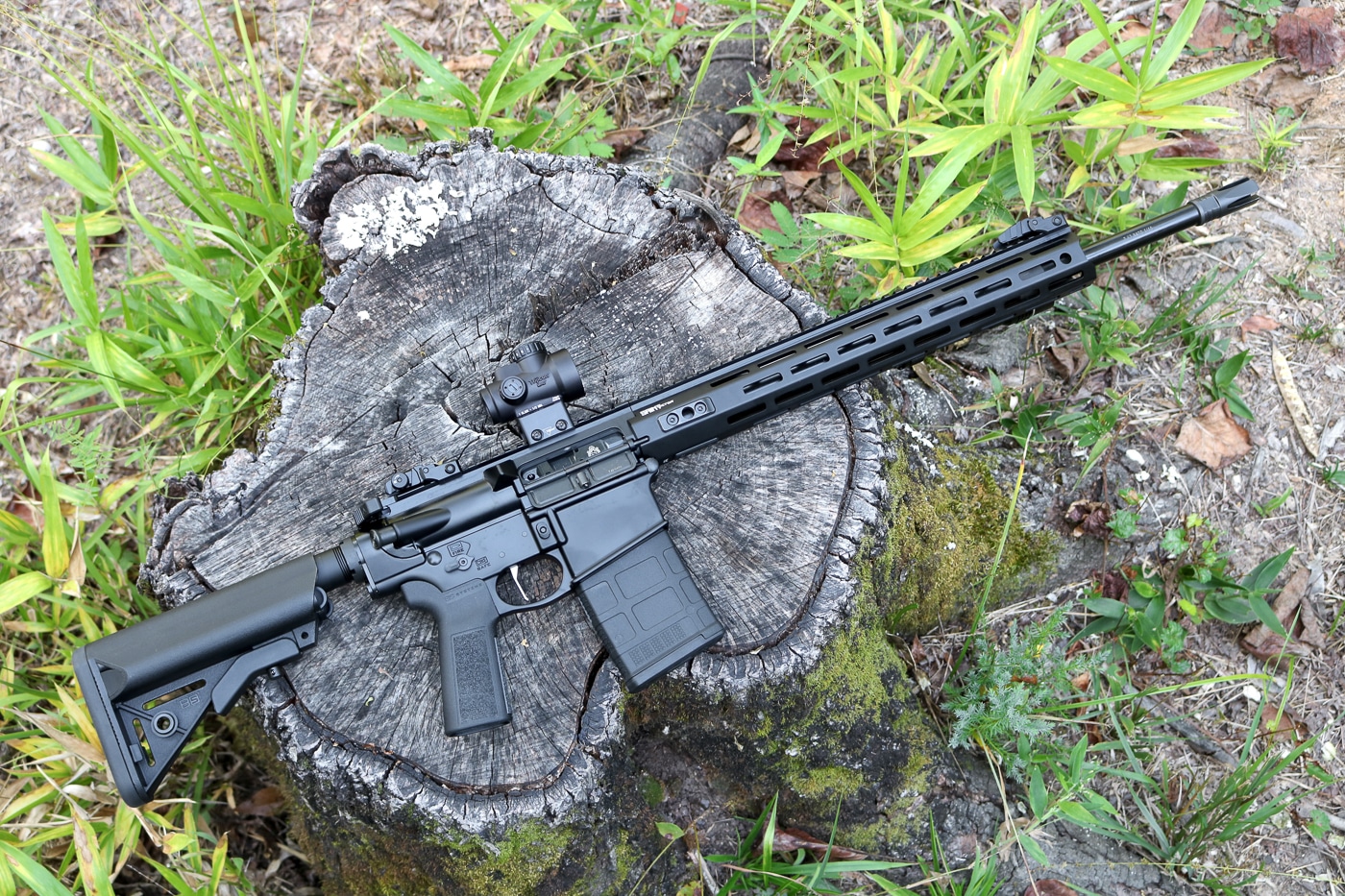 A Springfield Armory SAINT AR-10 rifle is photographed outdoors on a natural surface such as dirt or grass. The rifle’s black anodized finish, rail system, and adjustable stock are visible, reflecting the AR-10’s modern and utilitarian design. The lighting highlights the clean lines of the upper and lower receivers, showing the rifle’s refined build quality. The image conveys the platform’s balance between portability and power in a full-sized .308 rifle. Its position in an outdoor setting underscores real-world practicality for range use, hunting, or training. The photo emphasizes features like the free-float handguard and flat-top receiver. This visual supports the article’s focus on the AR-10 as a flexible, performance-oriented platform.