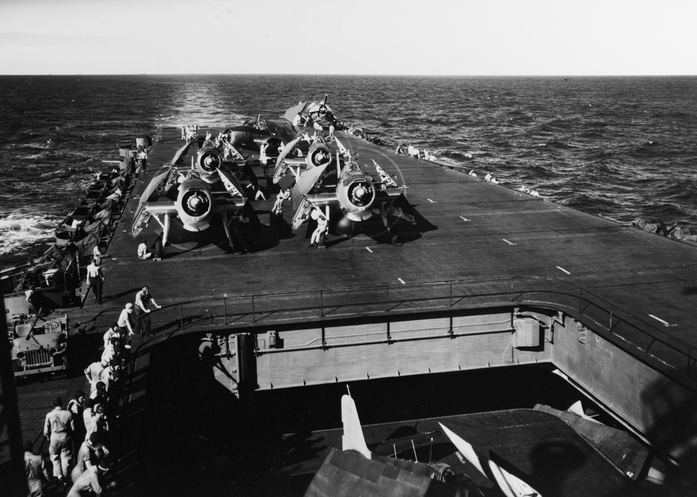This photo shows several TBM Avenger torpedo bombers lined up on the flight deck of USS Enterprise (CV-6) as they are prepared for flight in May 1944. Sailors and aviation mechanics are visible performing preflight checks, servicing engines, and loading torpedoes or bombs under the aircraft. Each Avenger displays U.S. Navy markings, and crew members are seen wearing flight gear and working with deck officers to ensure everything is ready for launch. The background reveals more of the ship’s deck and possibly other aircraft staged for upcoming missions. The teamwork between aircrew and maintenance personnel is evident in their organized activity. The scene highlights the vital preparation work that went into each combat sortie. These Avengers were a mainstay for anti-ship and bombing missions in the Pacific campaign.