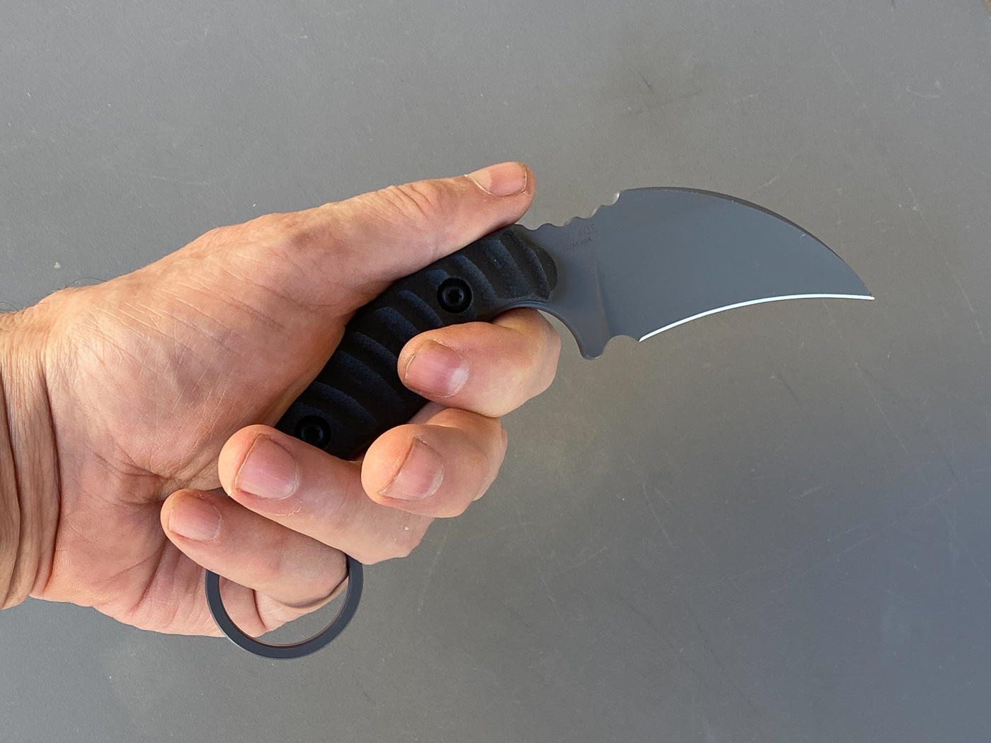 Photo showing the Toor Knives Karsumba R being held to demonstrate its ergonomic handle shape in a reverse grip. The curved G10 scales fit cleanly against the hand, while the retention ring allows fluid transition between grip styles. The reviewer’s hand placement highlights how the knife maintains control and balance regardless of orientation. This image supports the article’s section on design and ergonomics, emphasizing the knife’s purpose-built feel. The subtle texture on the handle and jimping on the spine show Toor’s attention to functional details. It’s a visual confirmation that the Karsumba R is made for real-world handling, not just display.