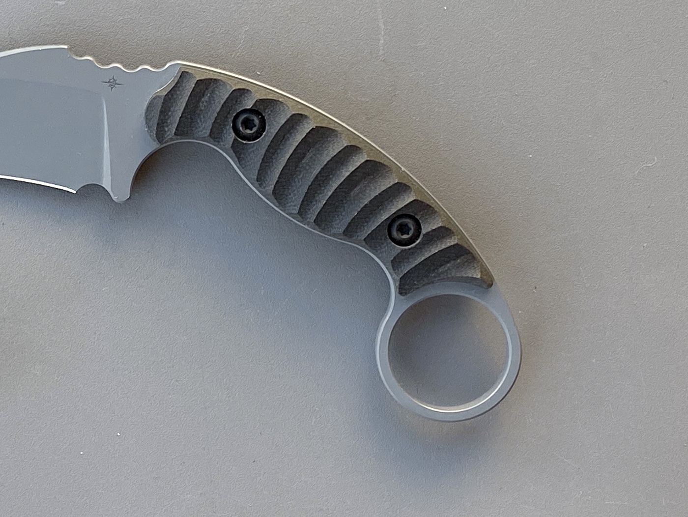 Close-up photo of the Toor Knives Karsumba R handle showing the textured G10 scales with Toor’s signature tread pattern. The surface provides excellent traction for wet or gloved hands while maintaining comfort during long handling. The finger groove and curved shape demonstrate the ergonomic focus of the design. Stainless Torx screws secure the scales to the full tang, and the retention ring is smoothly integrated at the end. The matte Phantom Grey finish complements the tactical styling without flash. This image supports the article’s section on build quality and control.
